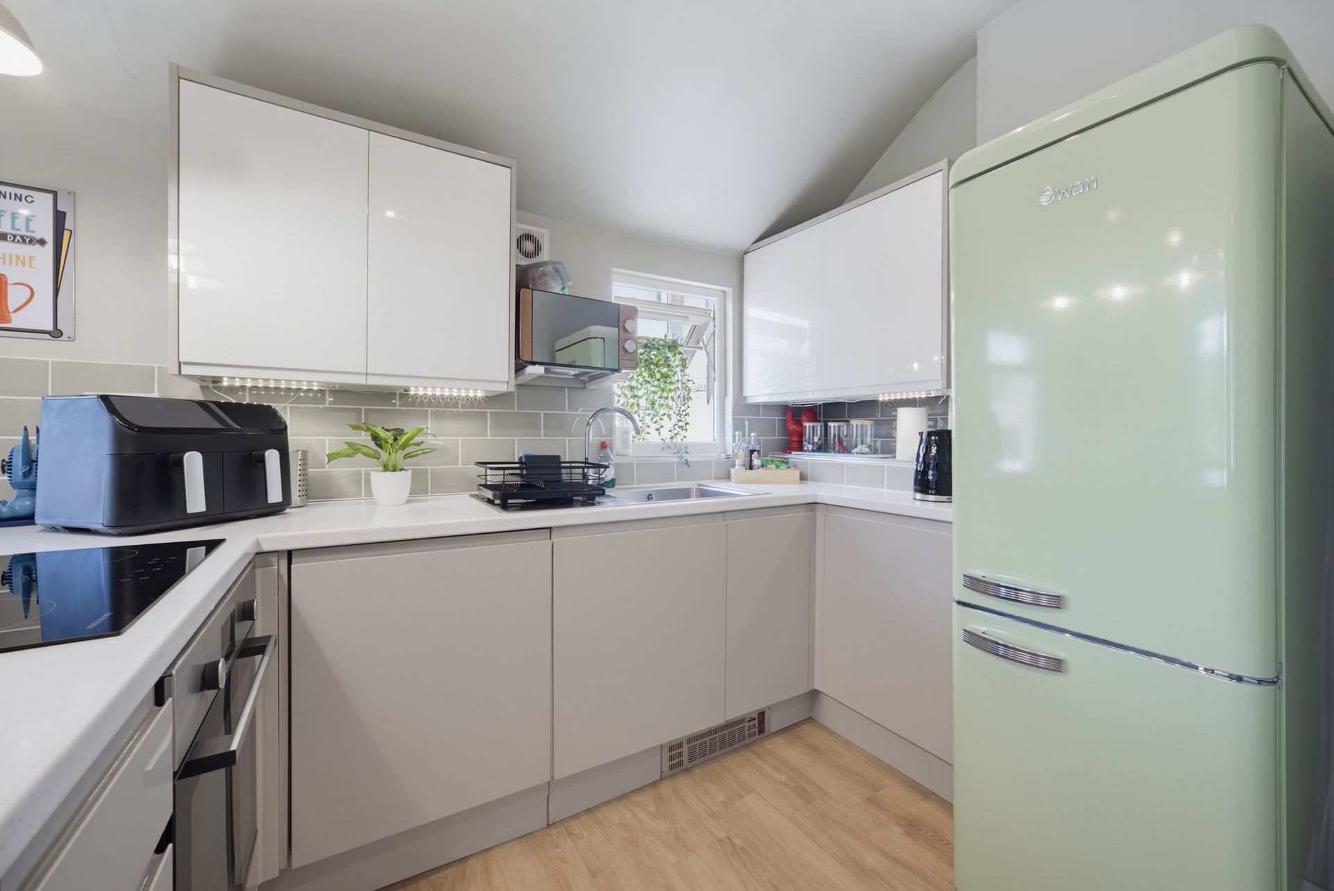 Bright modern kitchen with white cabinets, pale green fridge, and black countertop appliances