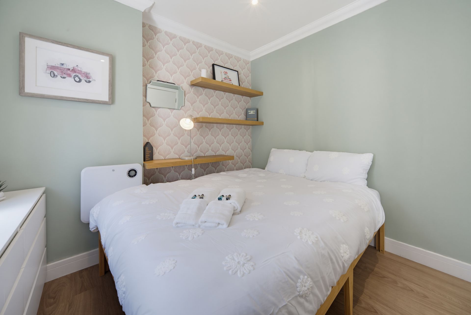 Bright bedroom with white bed, pale green walls, woven shelves, and framed art