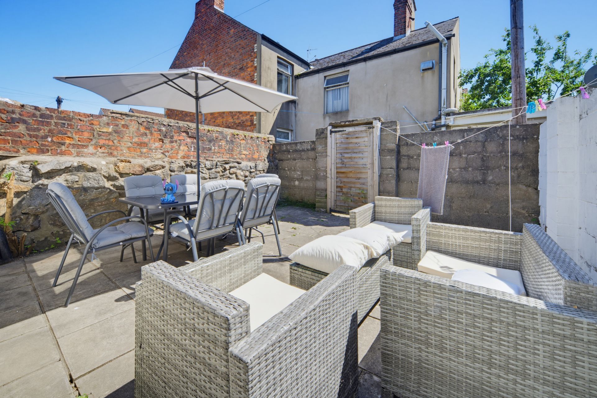 Patio with wicker seating, dining table, umbrella, and brick walls in a sunny courtyard