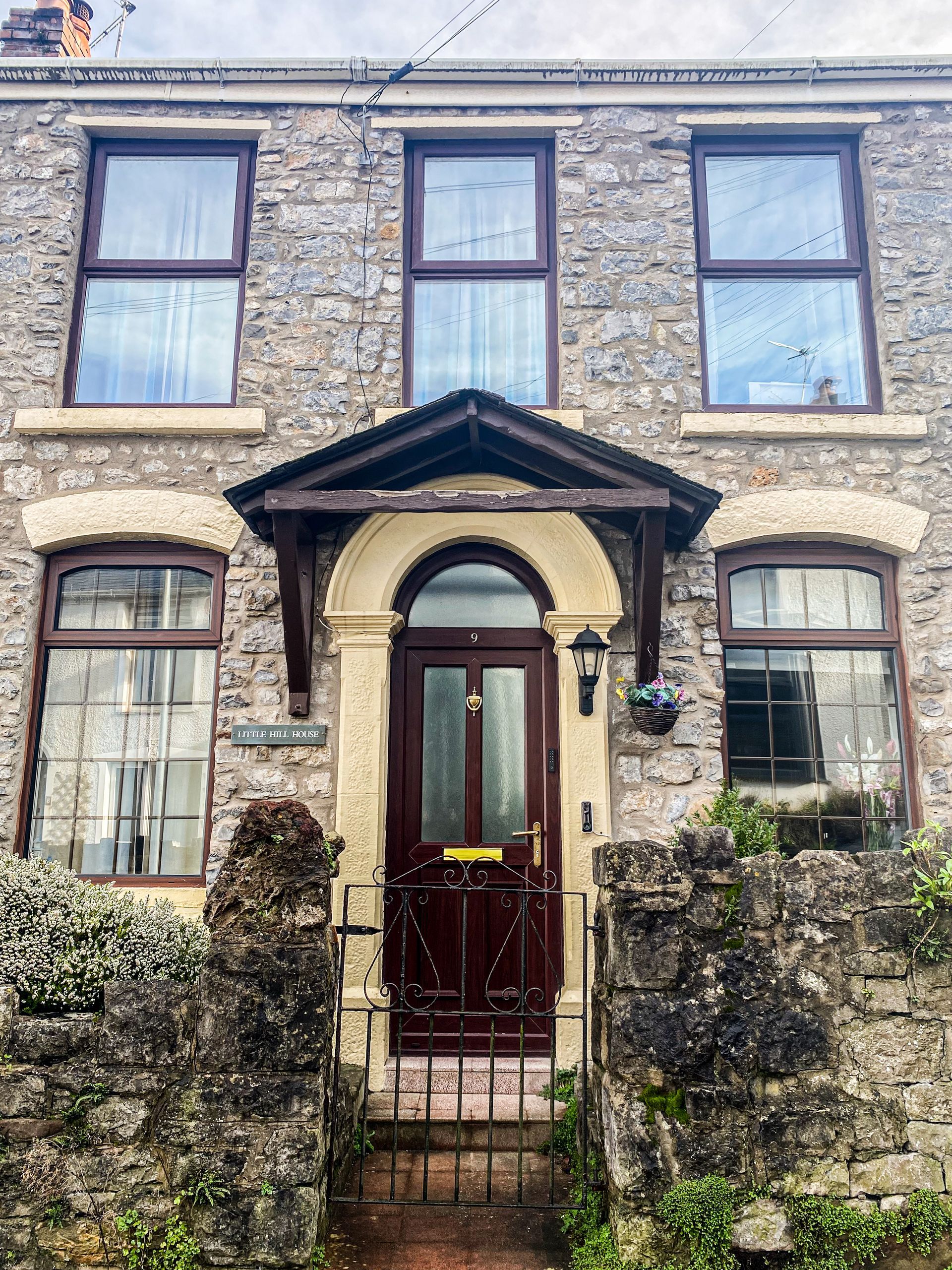 Stone terraced house with dark-framed windows, arched front door, and a gated front garden.