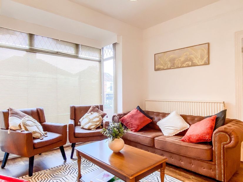 Bright living room with brown sofa, two chairs, coffee table, and large window with wavy blinds