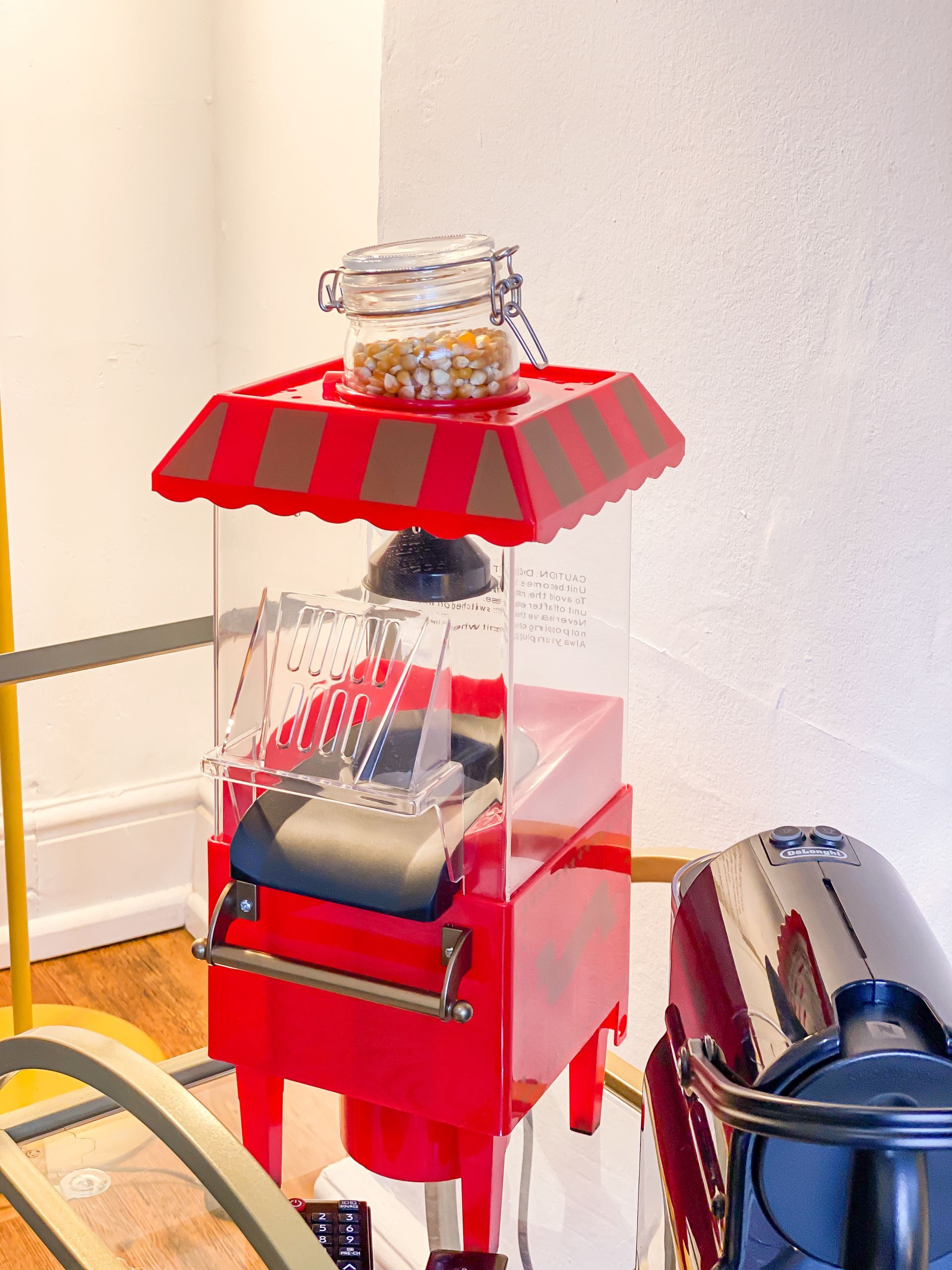 Red popcorn machine with clear bin and striped canopy next to a stainless appliance indoors