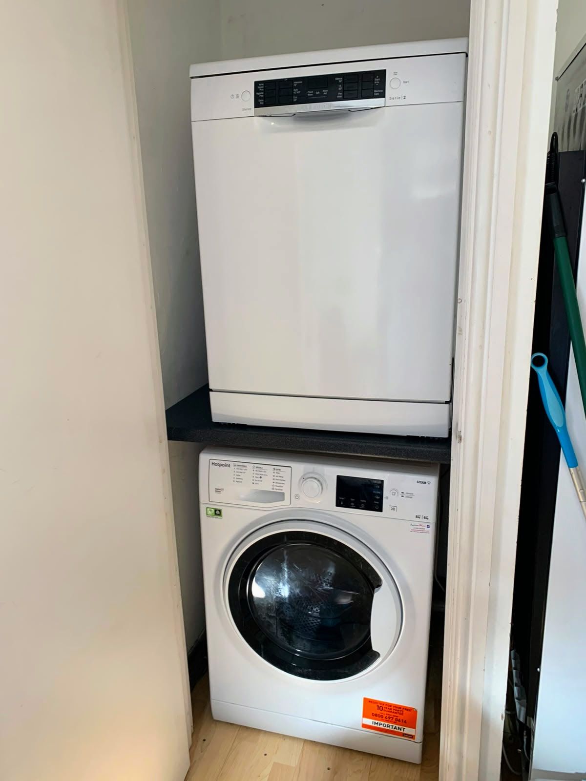 White dishwasher above a front-loading washing machine stacked in a narrow laundry nook