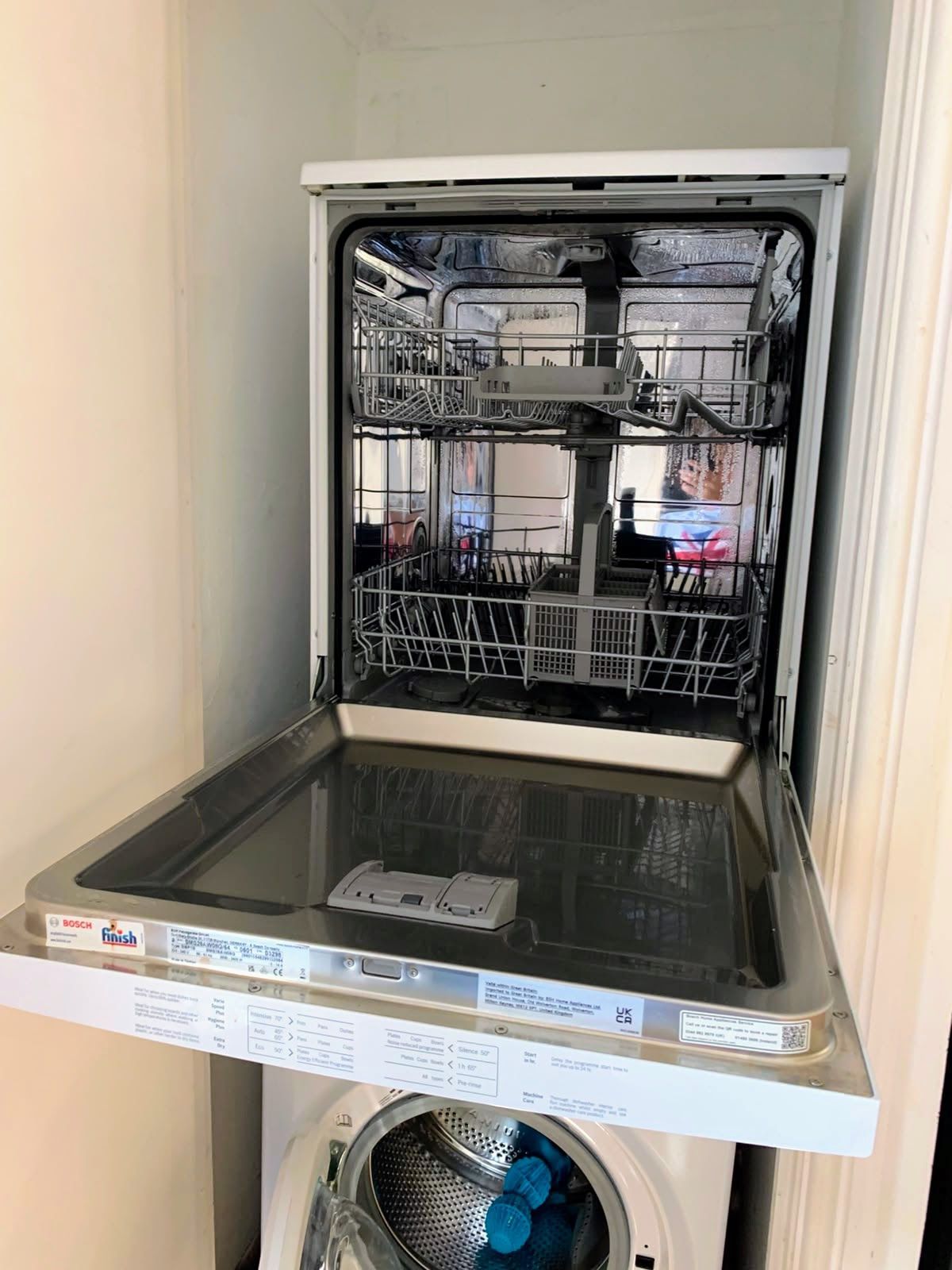 Open dishwasher with lower rack pulled out in a narrow kitchen alcove