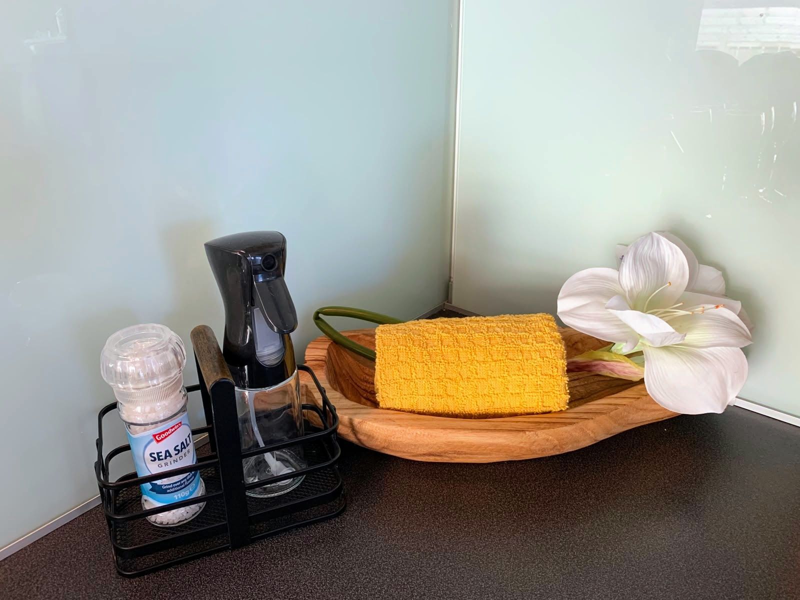 Bathroom countertop with soap, spray bottle, sponge, and white flower decor on a tray