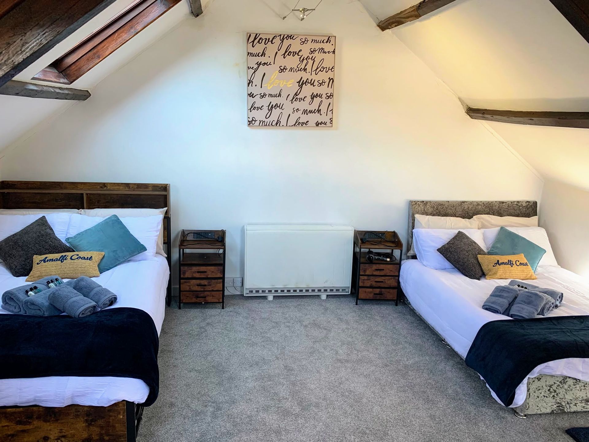 Small attic bedroom with two single beds, gray carpet, and exposed wooden beams.