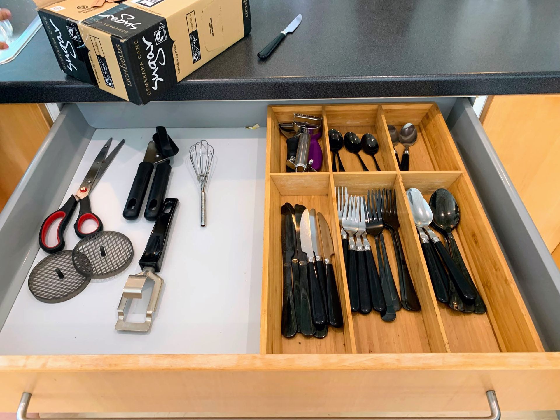 Drawer organizer with assorted tools and utensils in black, silver, and wood compartments.