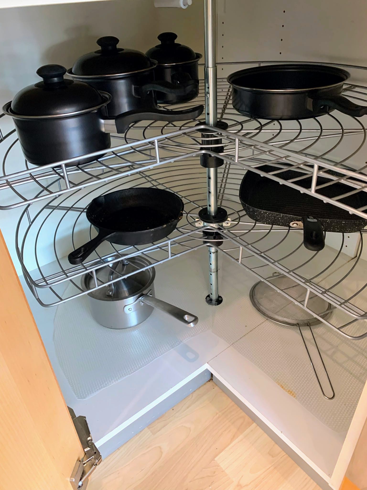 Rotating kitchen corner cabinet organizer with black pots, pans, and lids on wire shelves