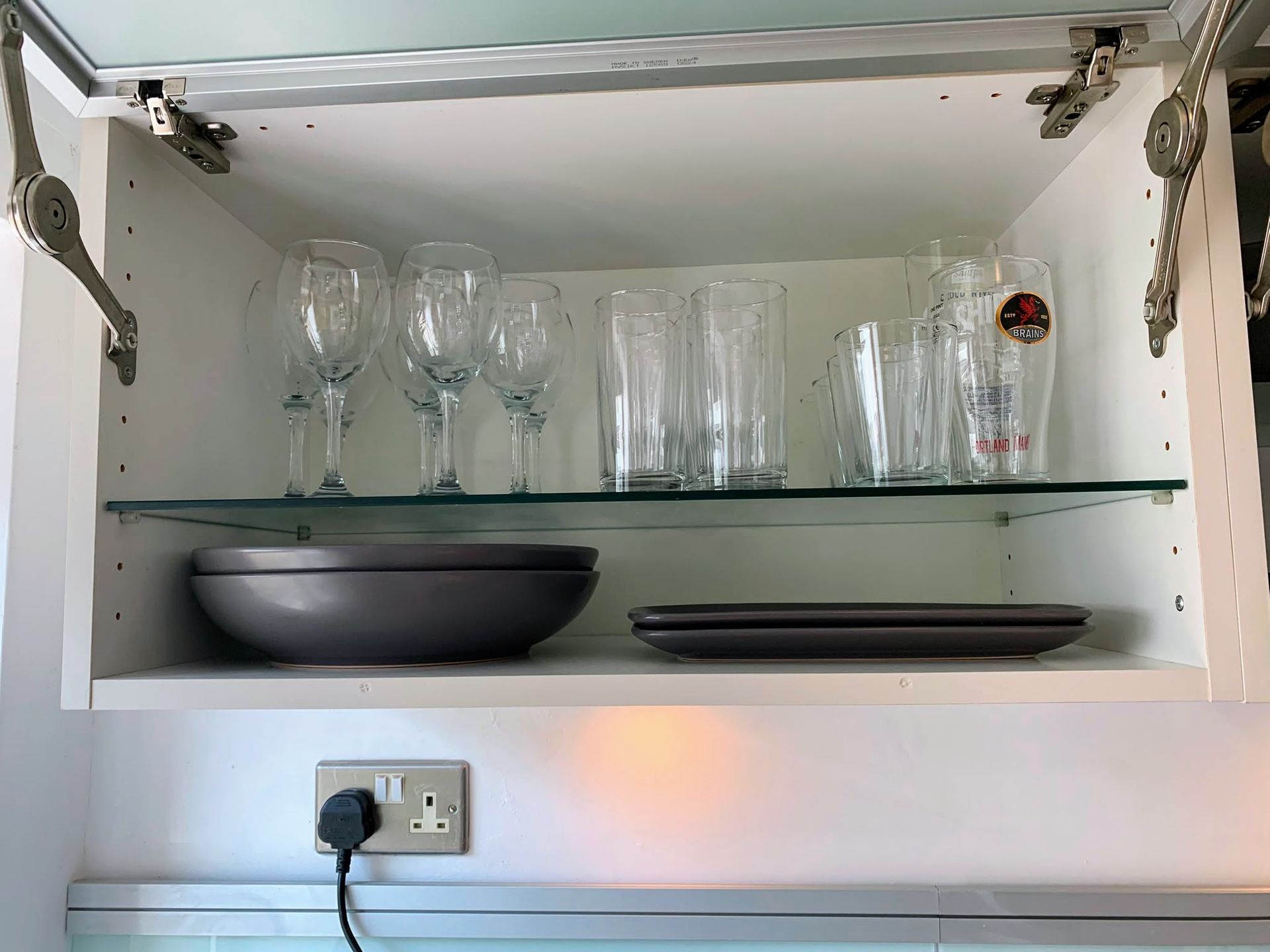 Open kitchen cabinet with glassware, bowls, and plates on shelves