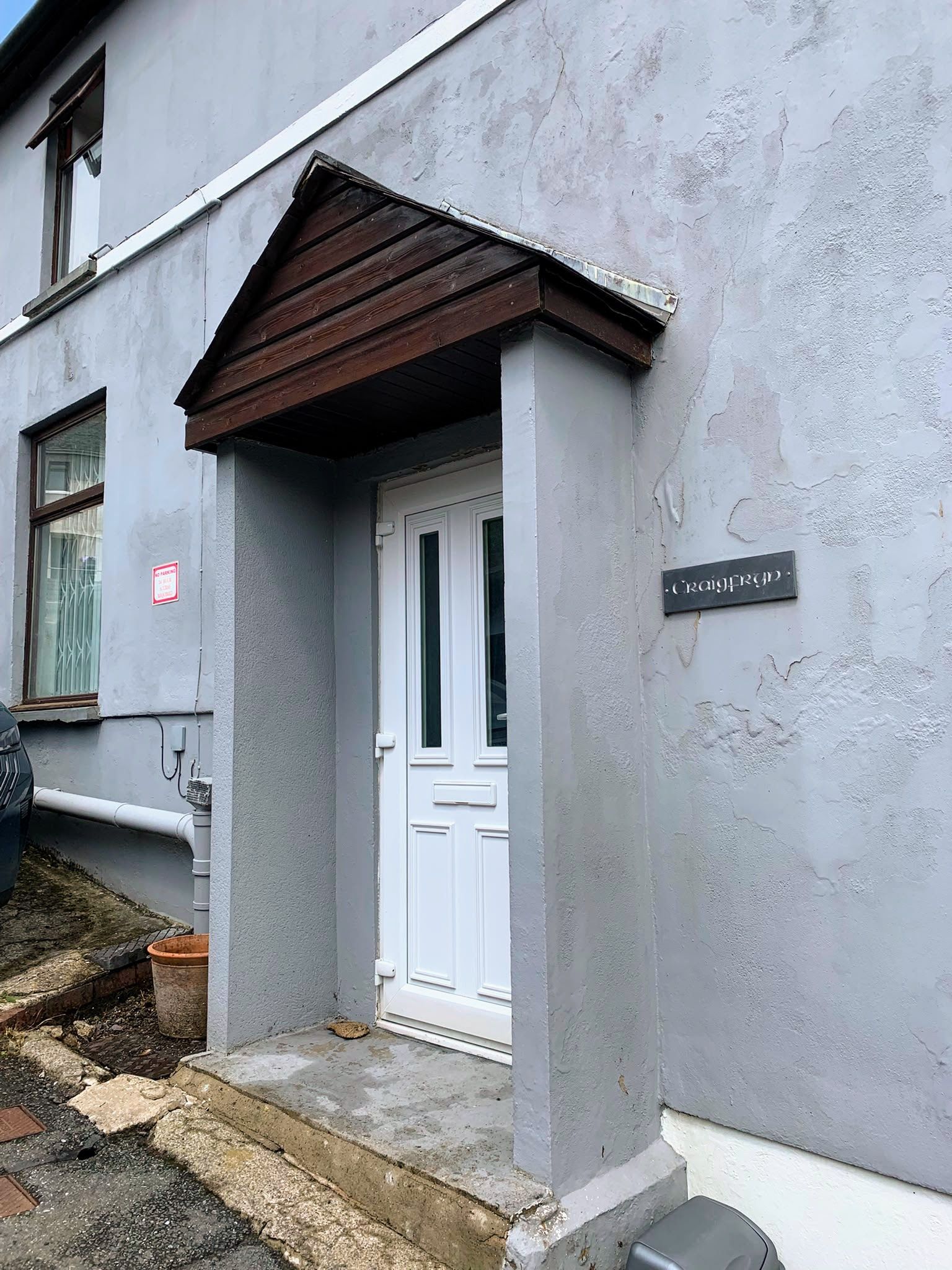 White front door under a brown awning on a gray house exterior.
