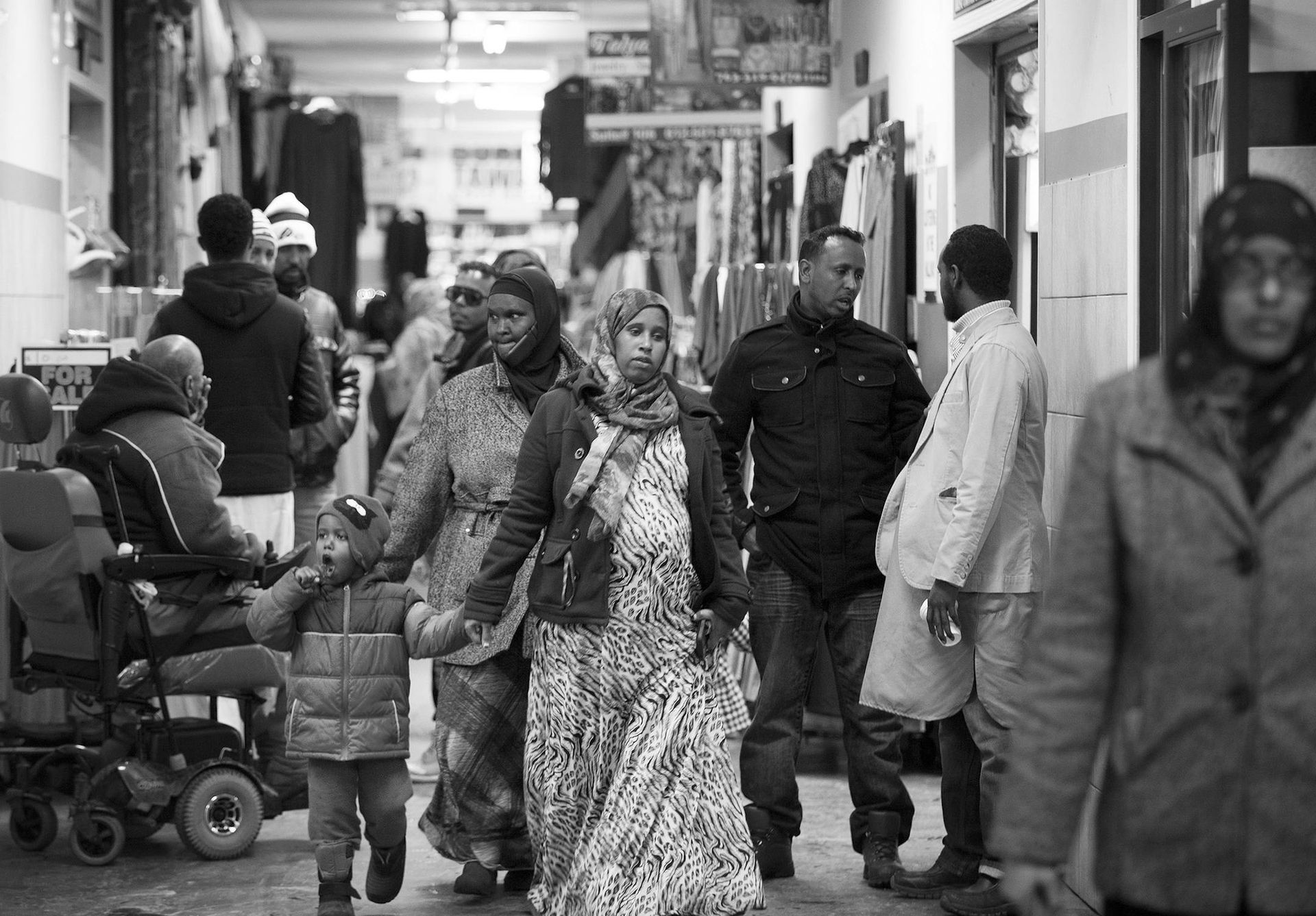 People walking in a crowded indoor market. A pregnant woman is holding hands with others. Black and white.