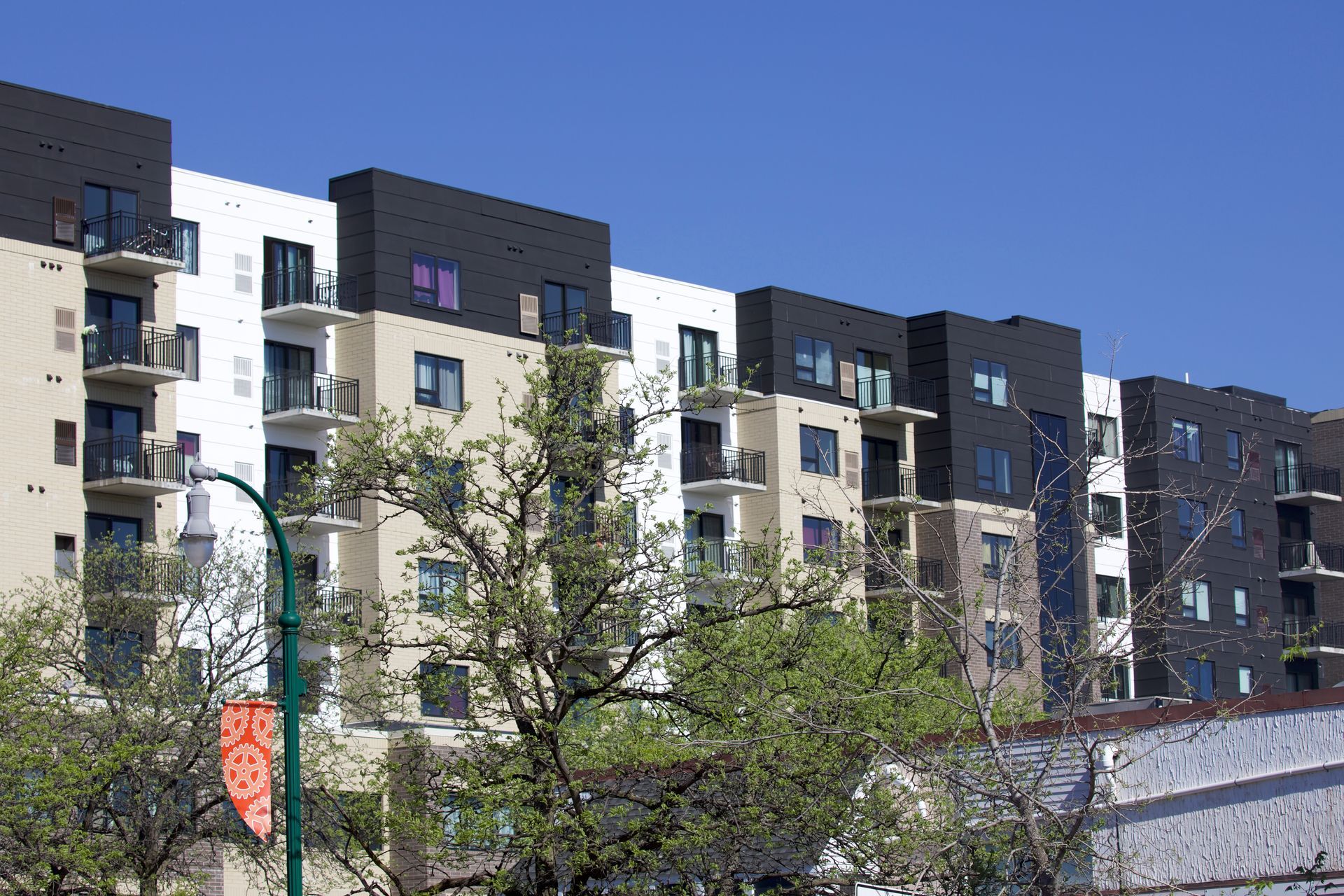 Multi-story apartment building with balconies and contrasting black and white panels under a clear blue sky.