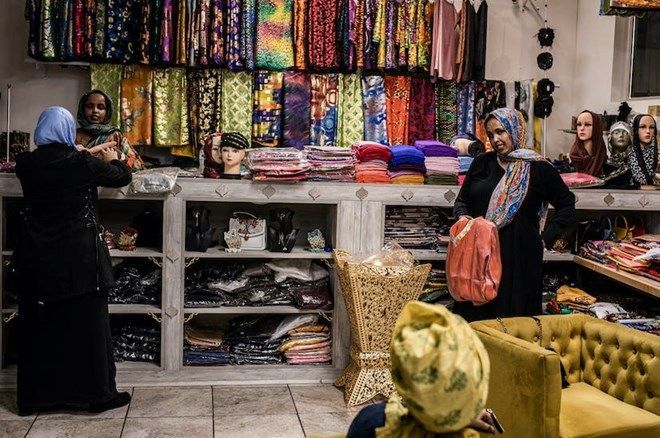 Women in a shop browsing colorful fabrics and scarves. Display shelves and a yellow sofa.