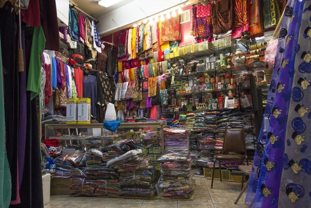 Inside a shop, fabric, shawls and trinkets are displayed. Shelves and racks filled with items.