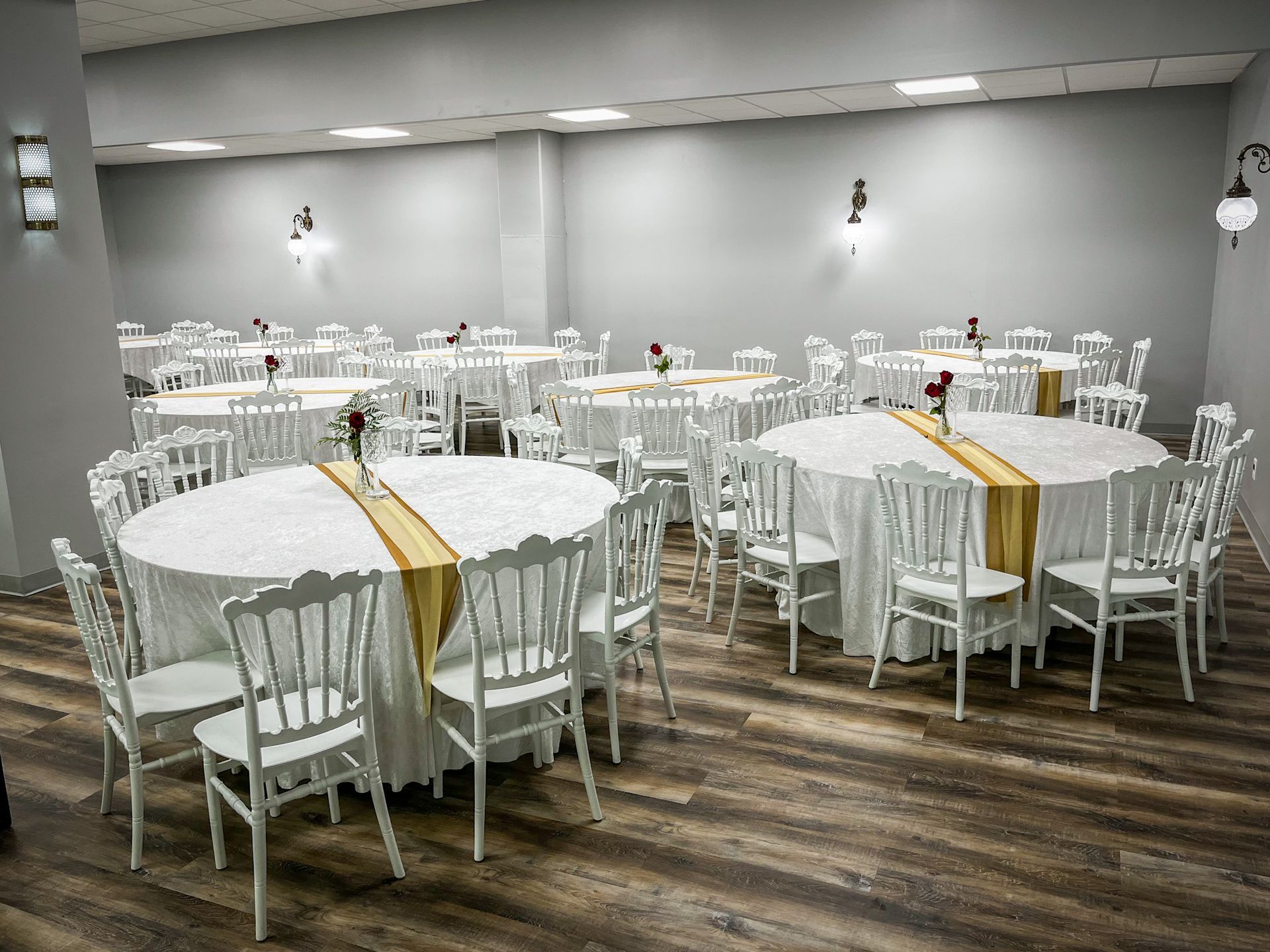 Empty banquet hall with round tables, white chairs, and gold table runners, ready for an event.