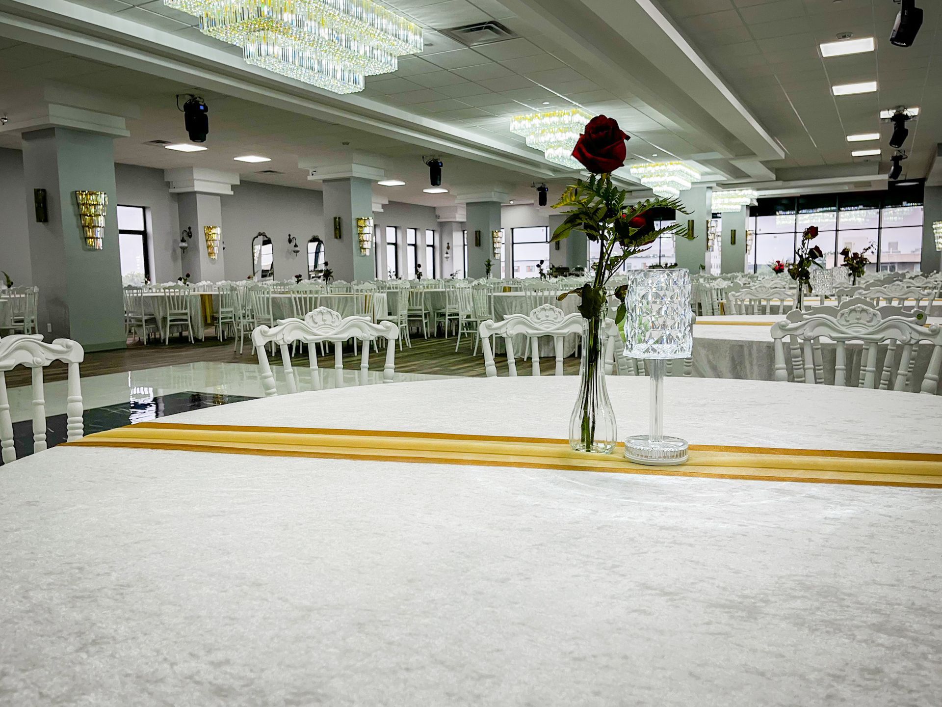 Elegant banquet hall with round tables, white decor, and a rose centerpiece.