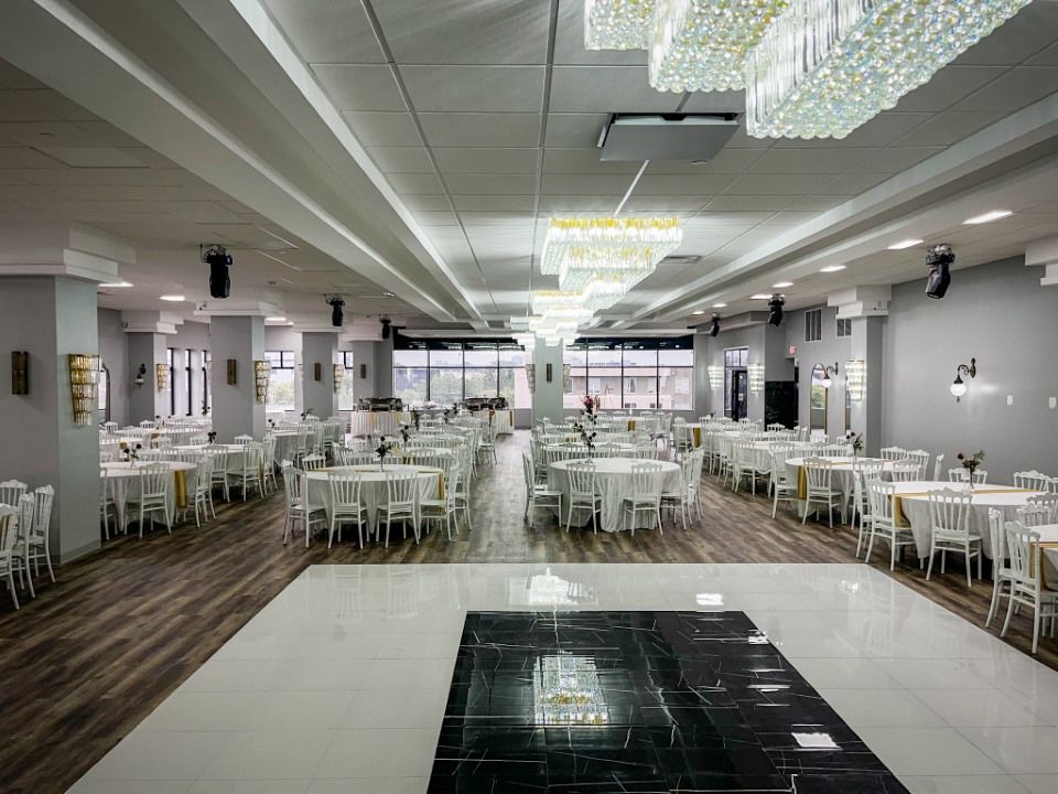 Elegant banquet hall with tables set for a celebration, featuring a dark dance floor, chandeliers, and neutral decor.