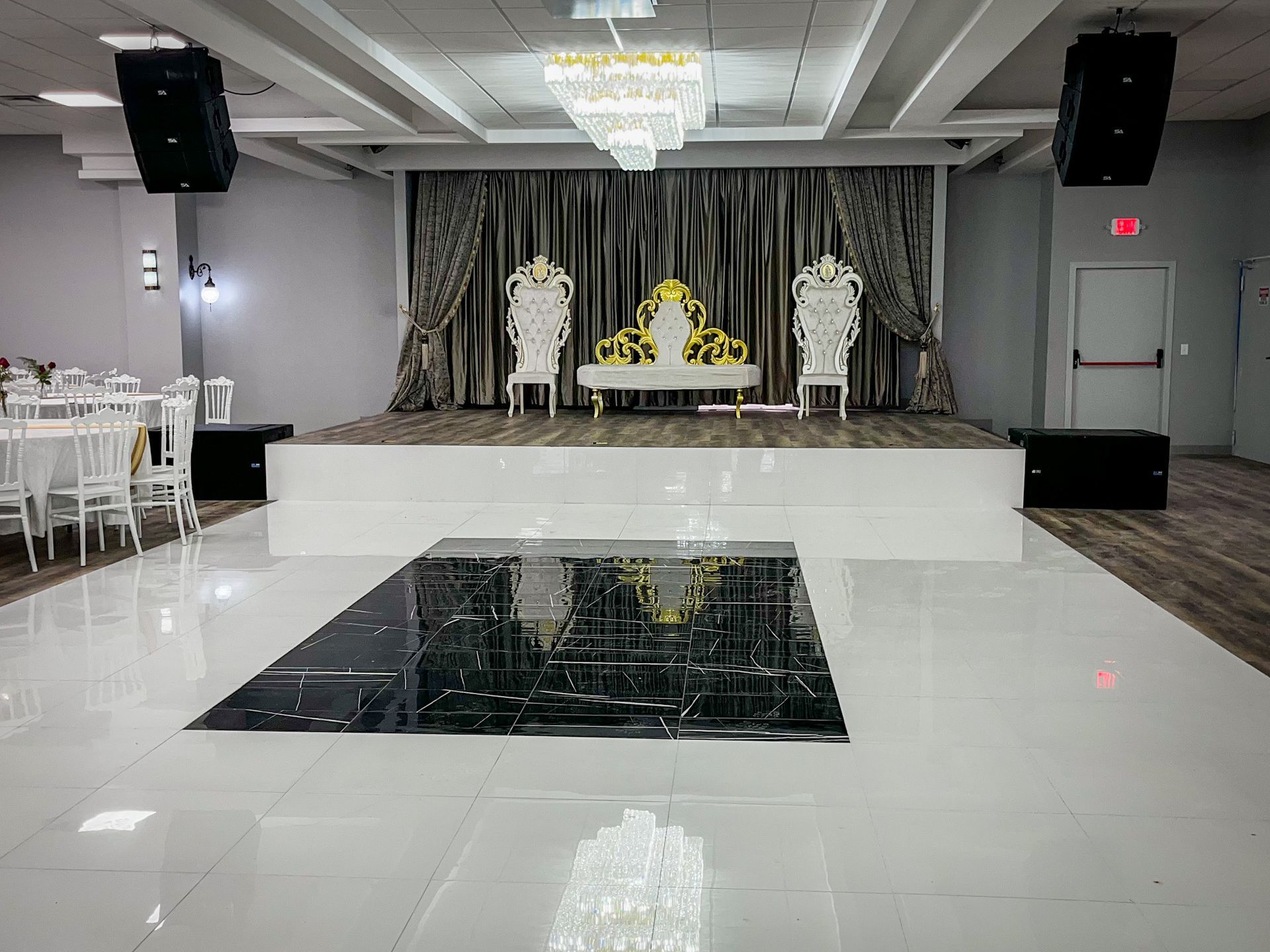 A ballroom with a stage, seating, dance floor, speakers, and chandeliers.
