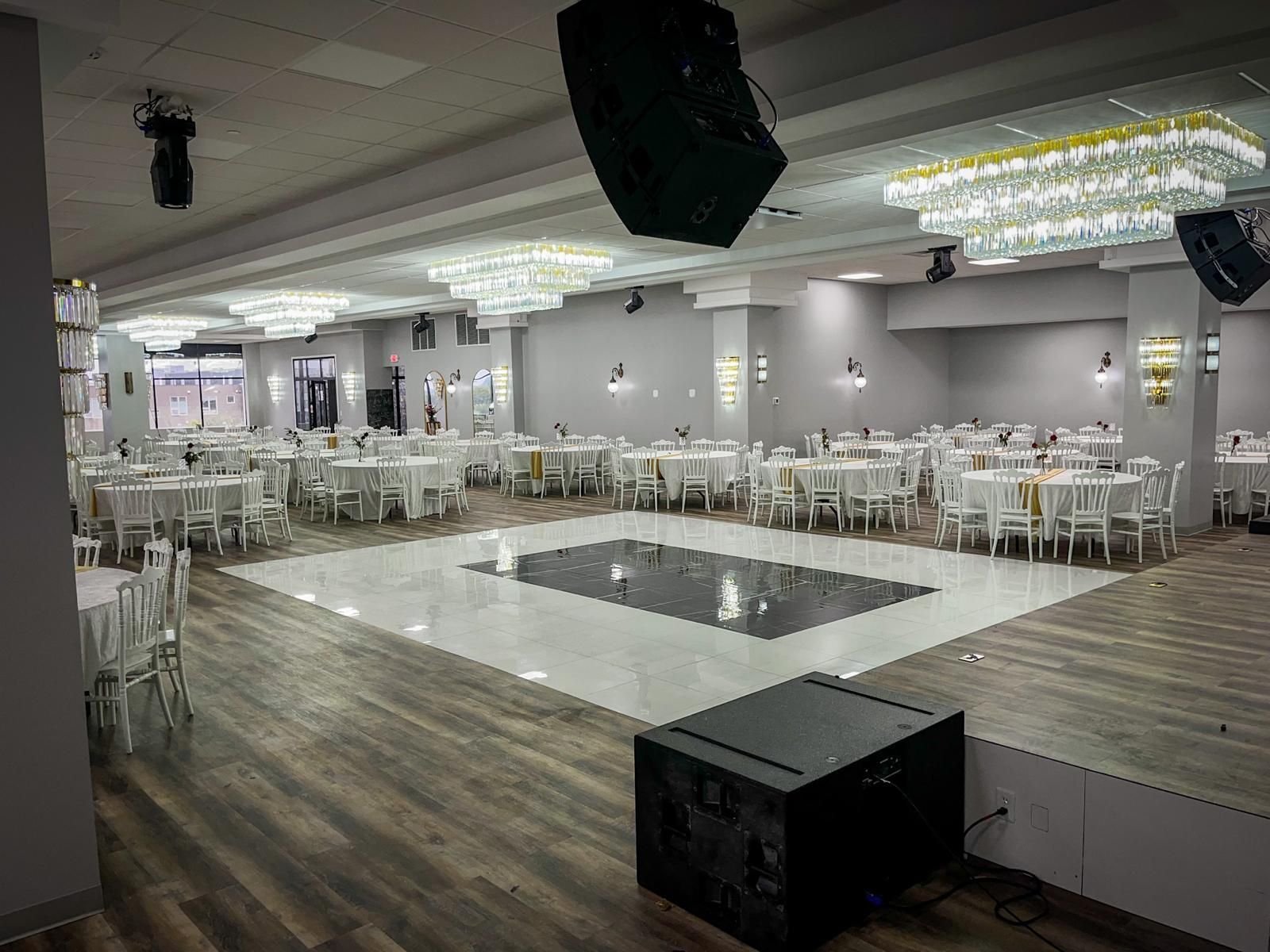 Large event hall with white tables, dance floor, chandeliers, and sound equipment.