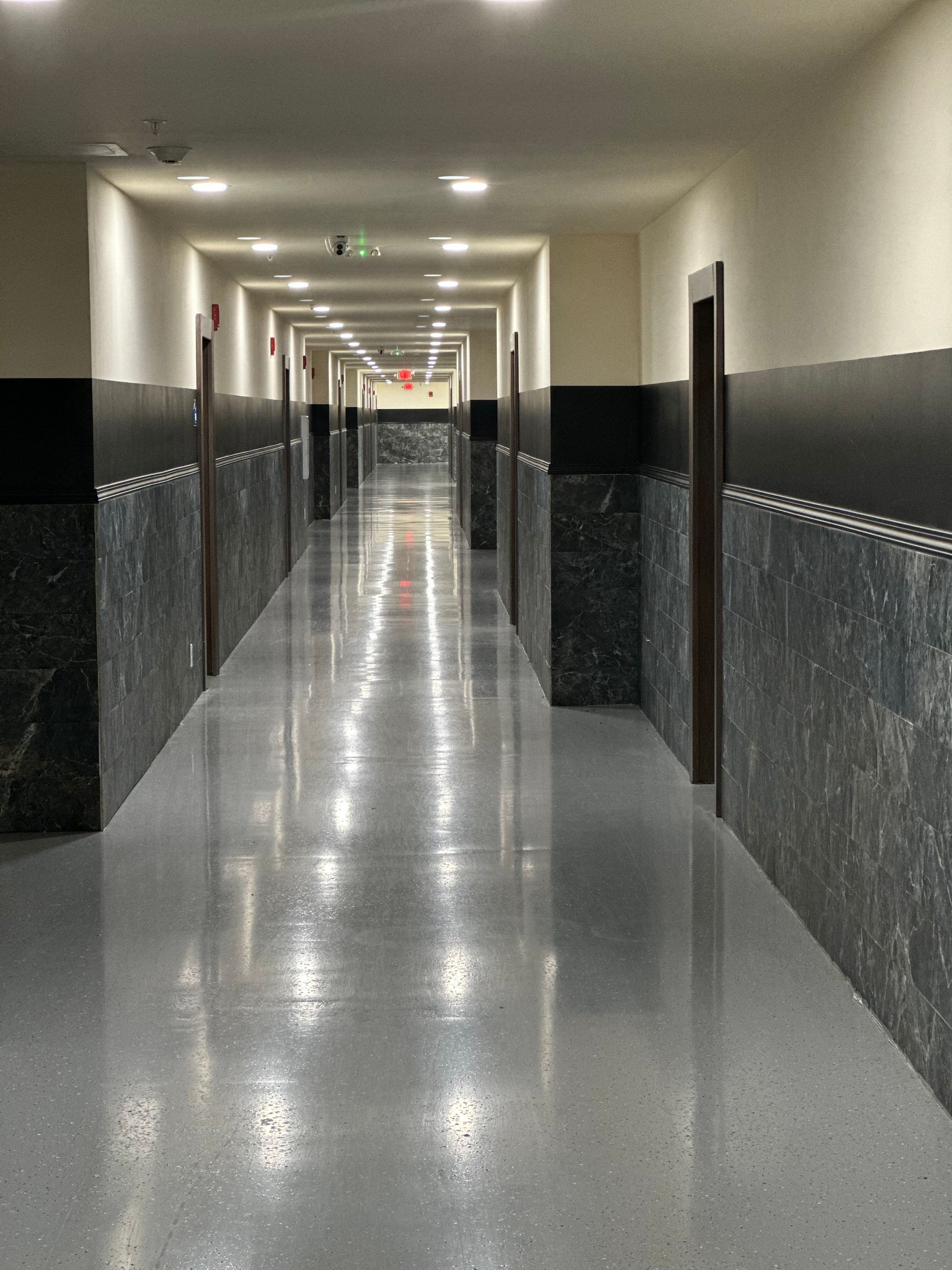Long, shiny hallway with doors, marble wainscot, and overhead lights.