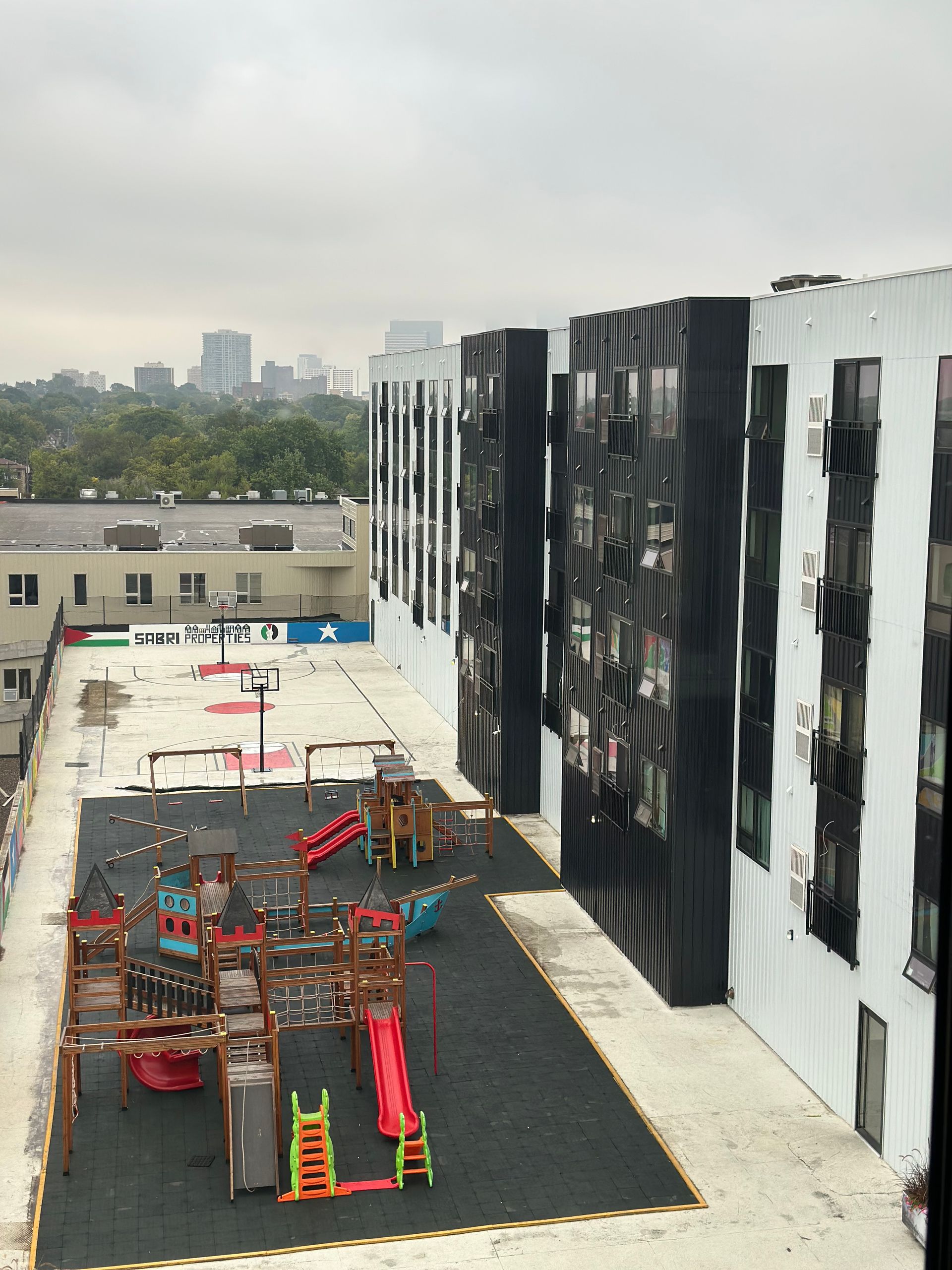 Playground on a rooftop next to a tall building on an overcast day.