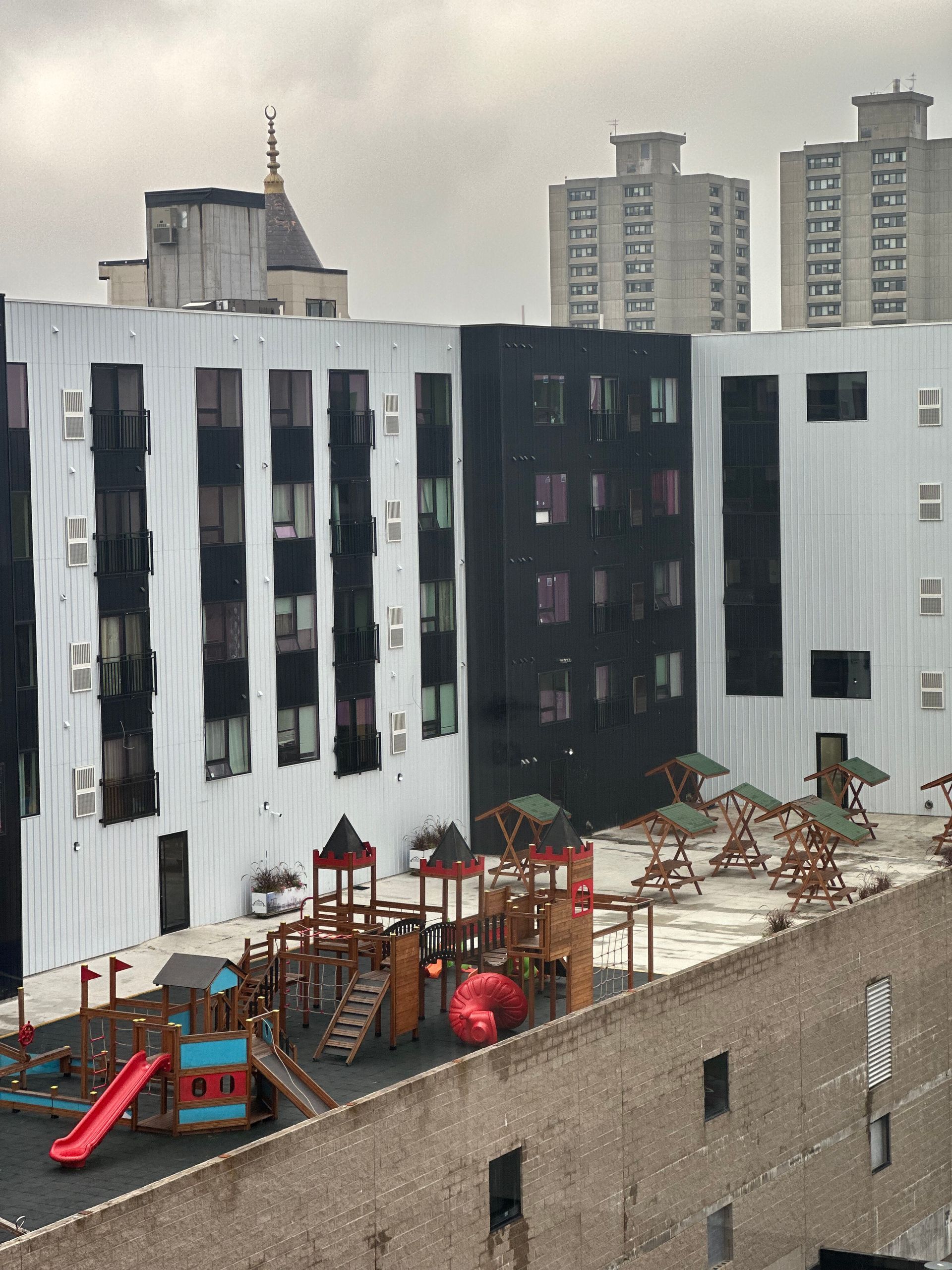 Playground on a rooftop deck of a building with black and white facade, cloudy sky.