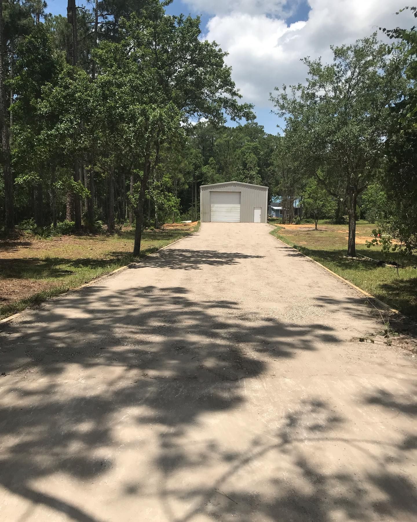 A dirt road leading to a garage surrounded by trees