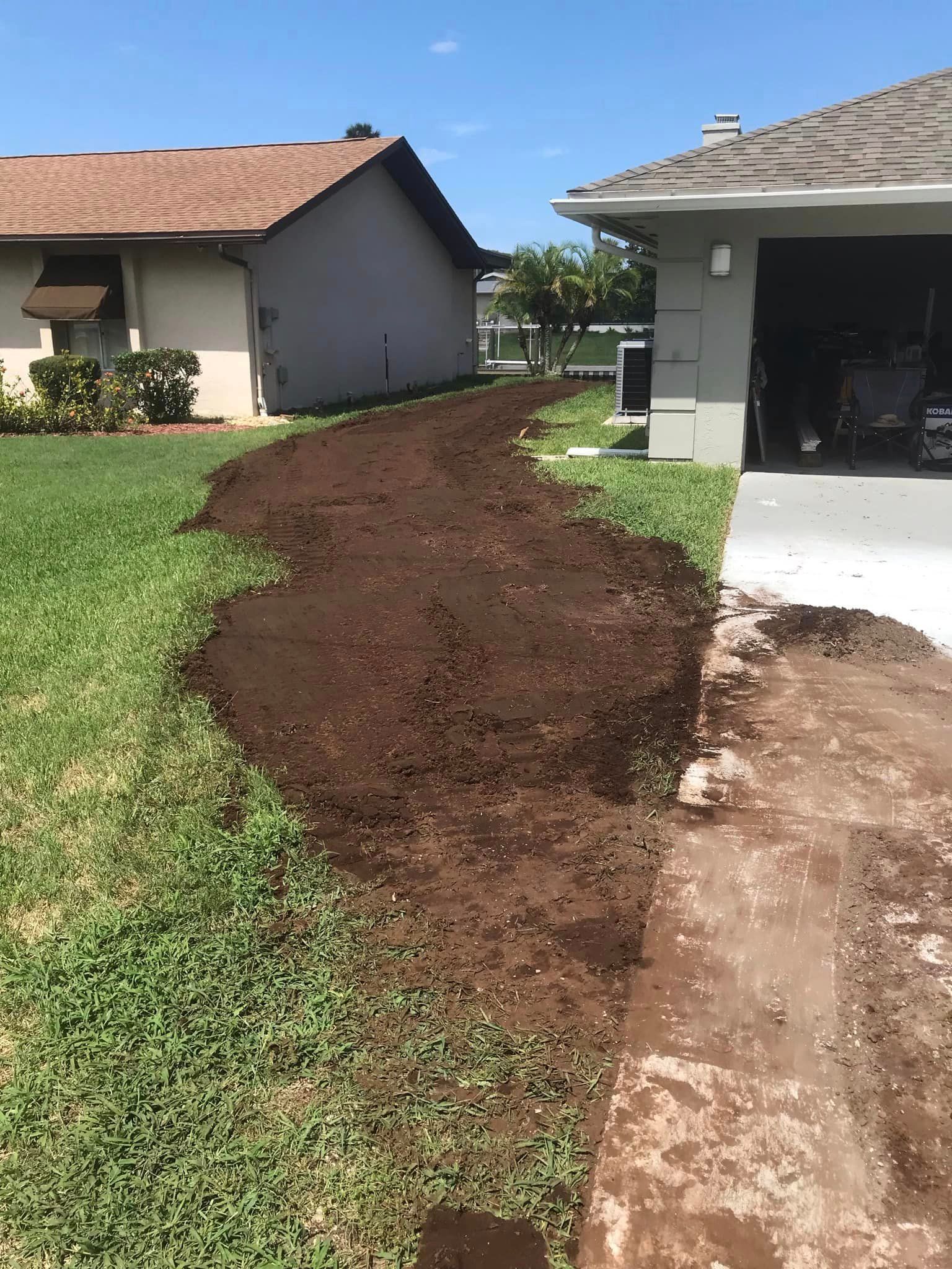 A dirt path leading to a house with a garage in the background.