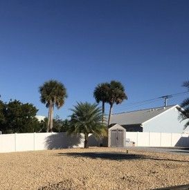A house with a white fence and palm trees in front of it.