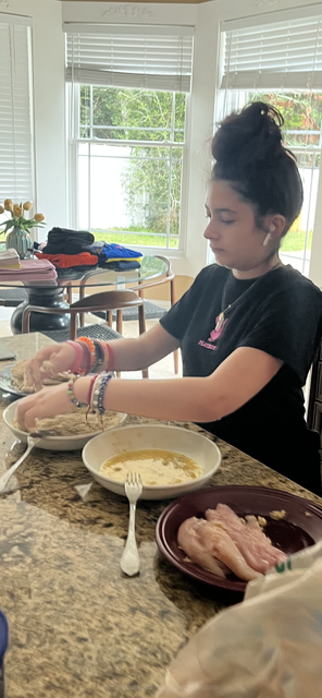 A young girl is sitting at a table preparing food.