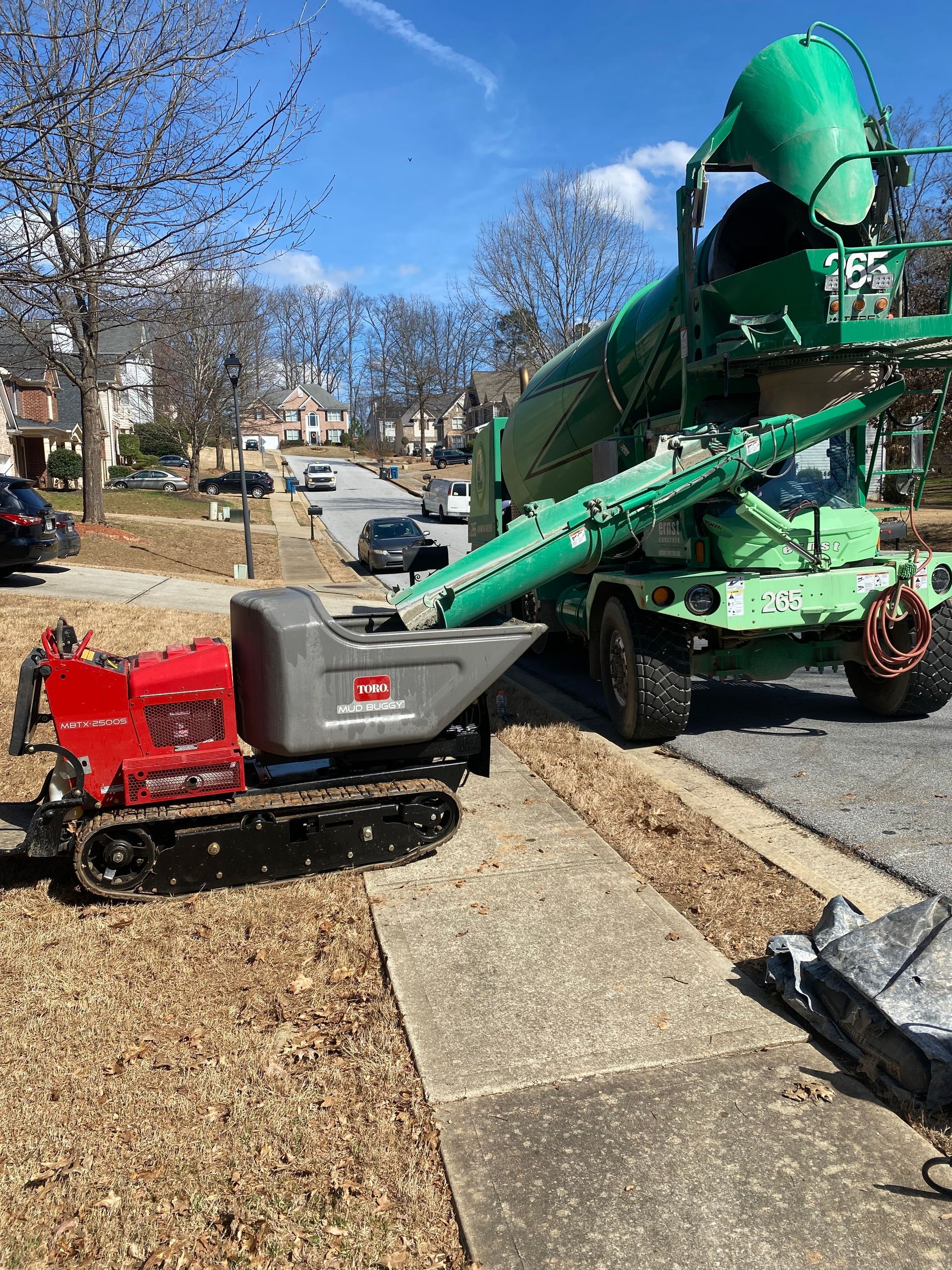 Red and gray mini-dumper receiving debris from a green debris truck on a residential street. Sunny day.
