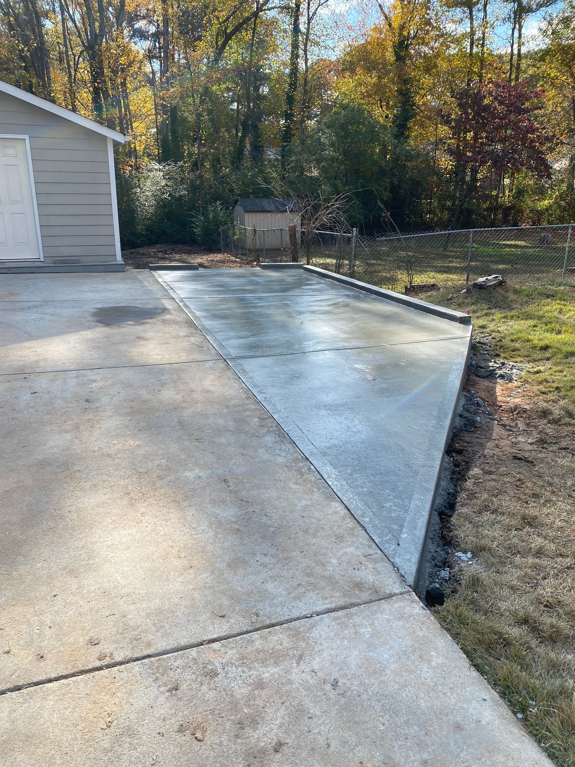 Newly poured concrete driveway extension next to an existing concrete driveway, near a garage and lawn.