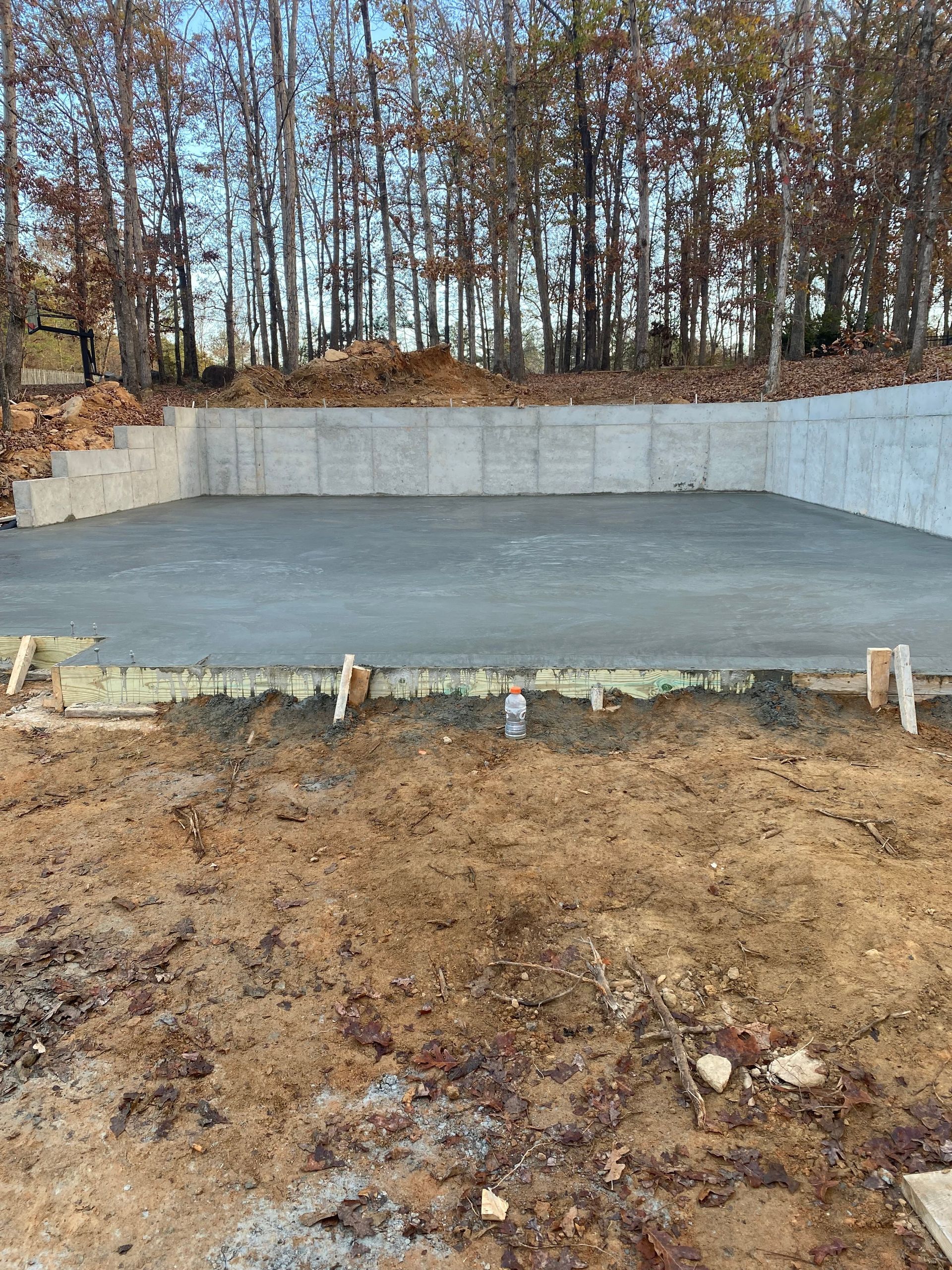 Concrete foundation of a building under construction, set in dirt, with trees in the background.