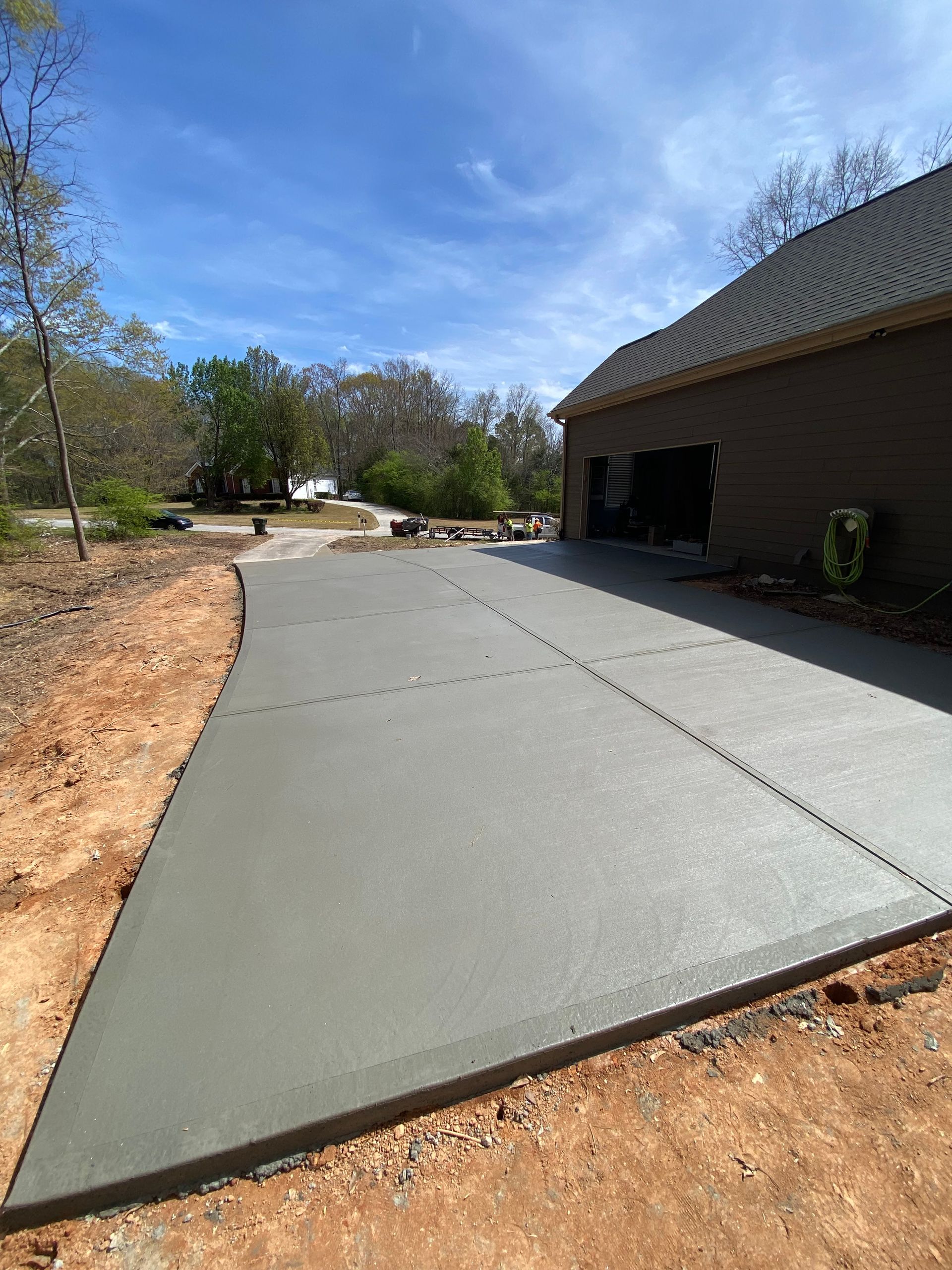 Newly poured concrete driveway leading to a brick house with a garage, on a sunny day.