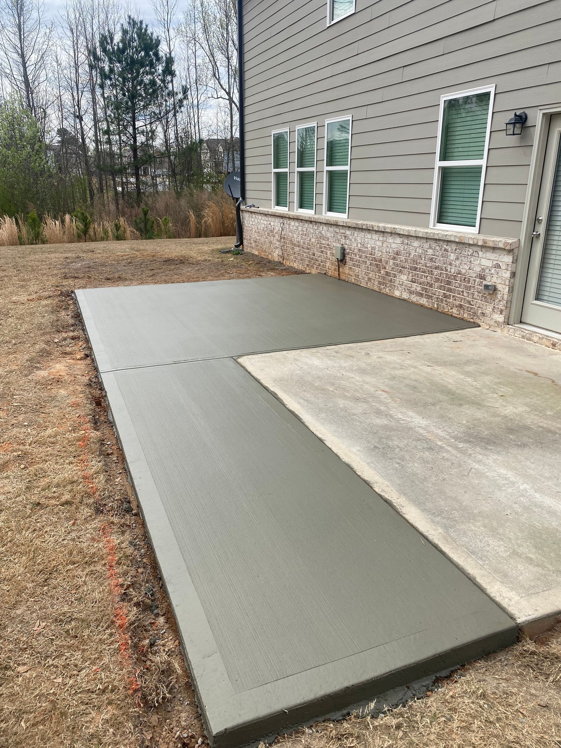 Freshly poured concrete patio against a house with brick foundation.