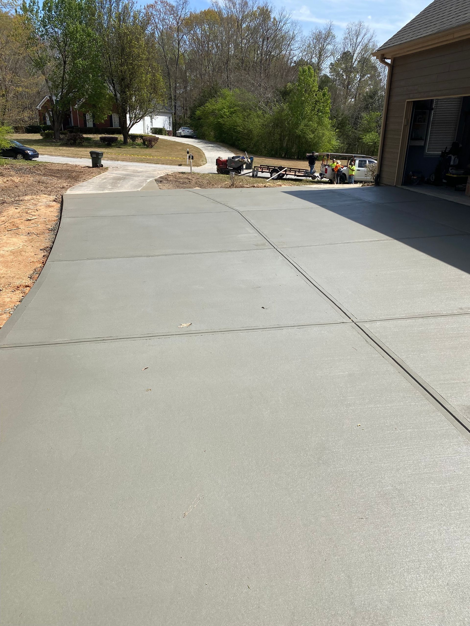 Newly poured concrete driveway with fresh footprints, leads to a brick garage.