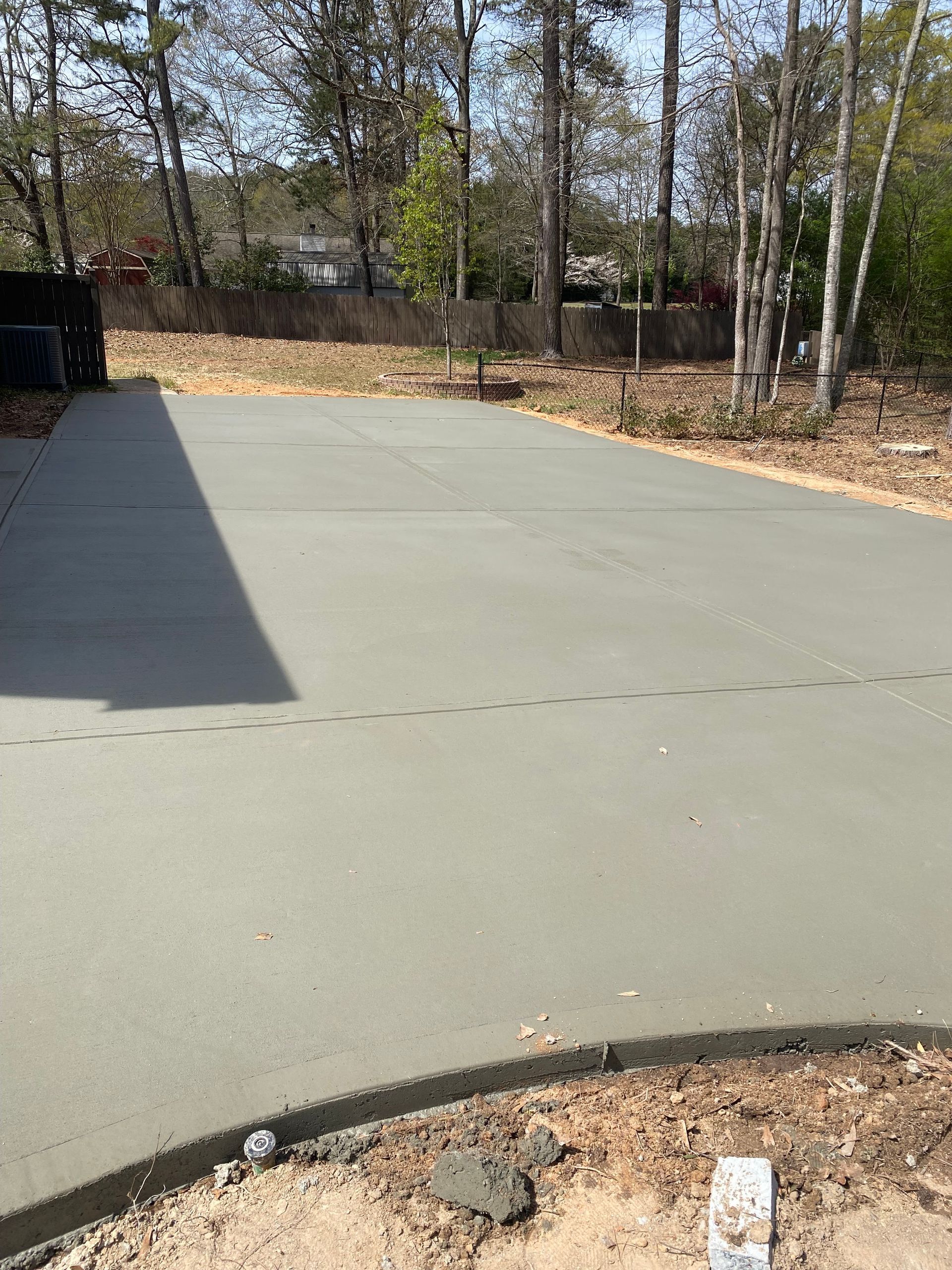 Newly poured gray concrete driveway in a wooded area.