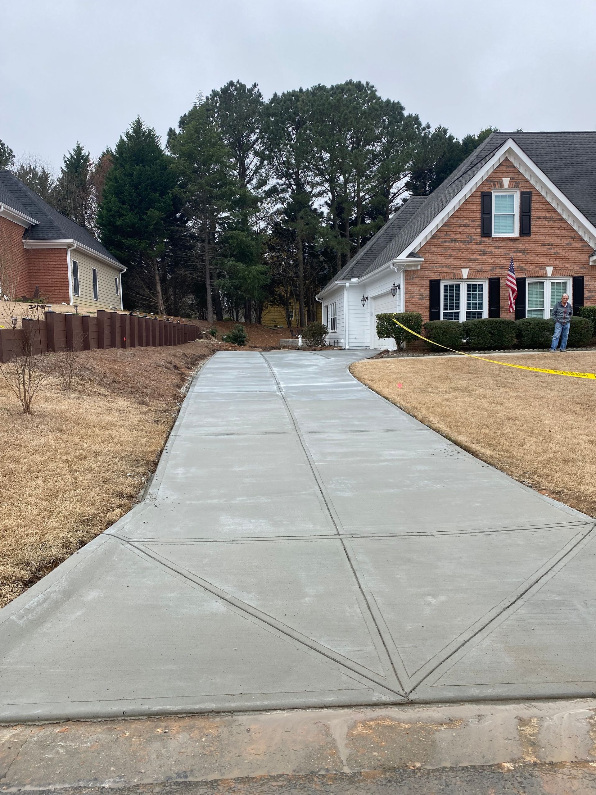 Newly poured concrete driveway leading to a brick house on a cloudy day.