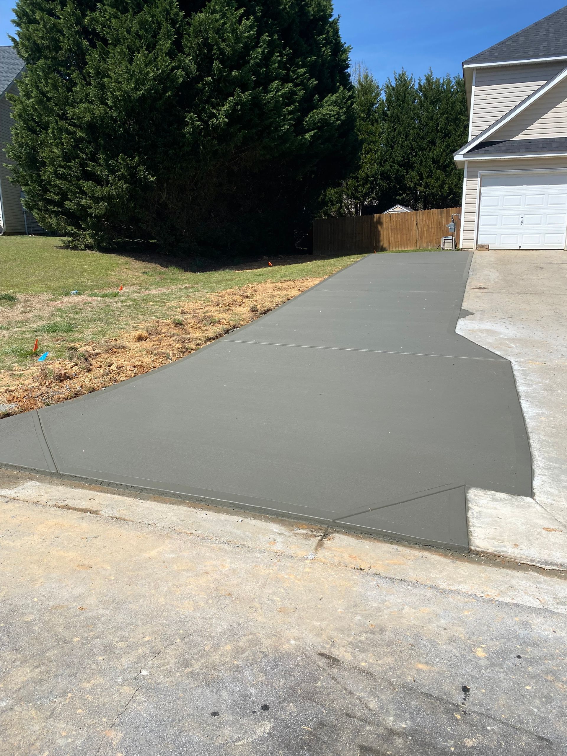 Freshly poured gray concrete driveway leading to a white garage door, with green lawn and trees in the background.
