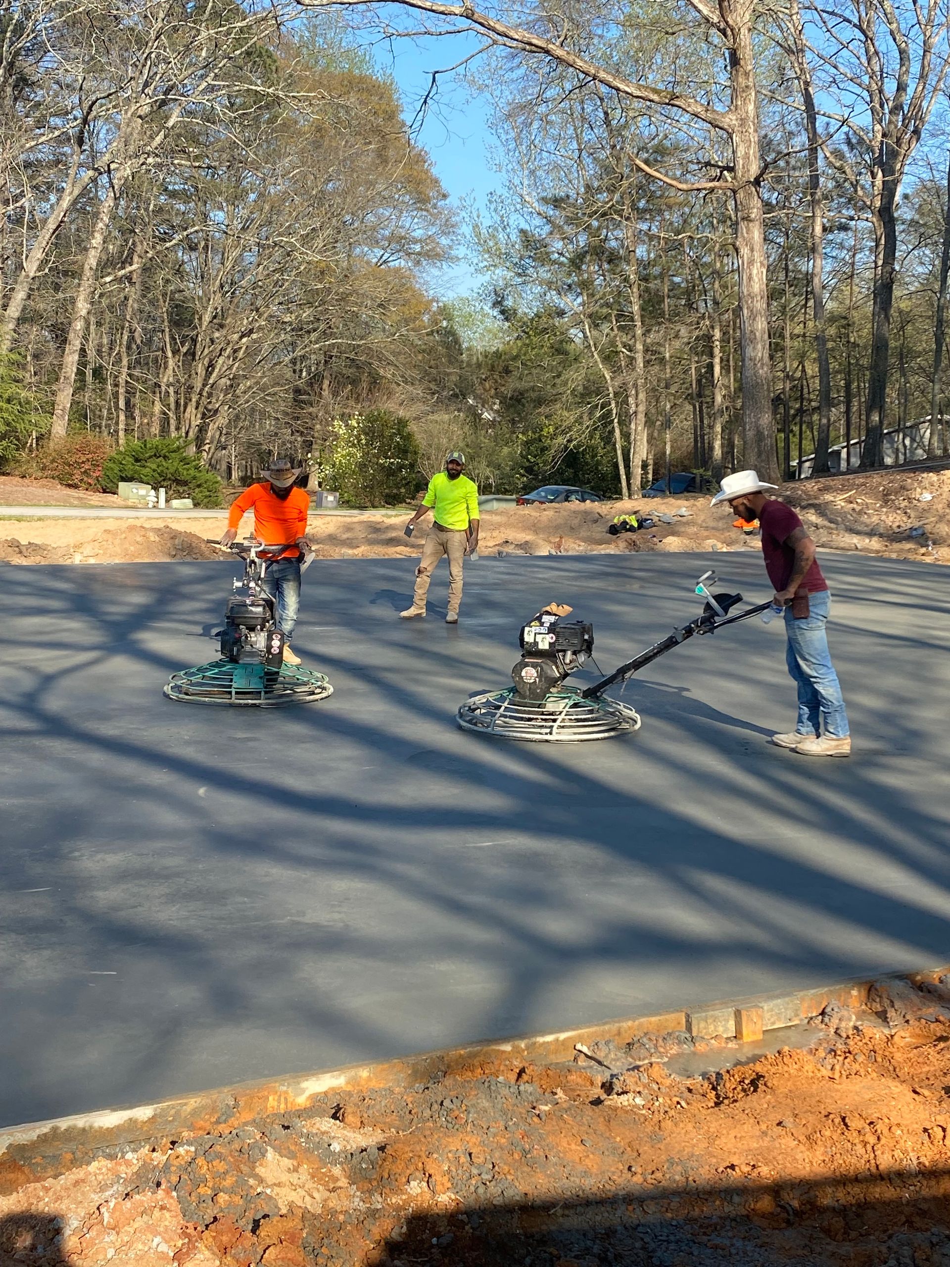 Three workers smoothing a freshly poured dark concrete surface with power trowels outdoors.