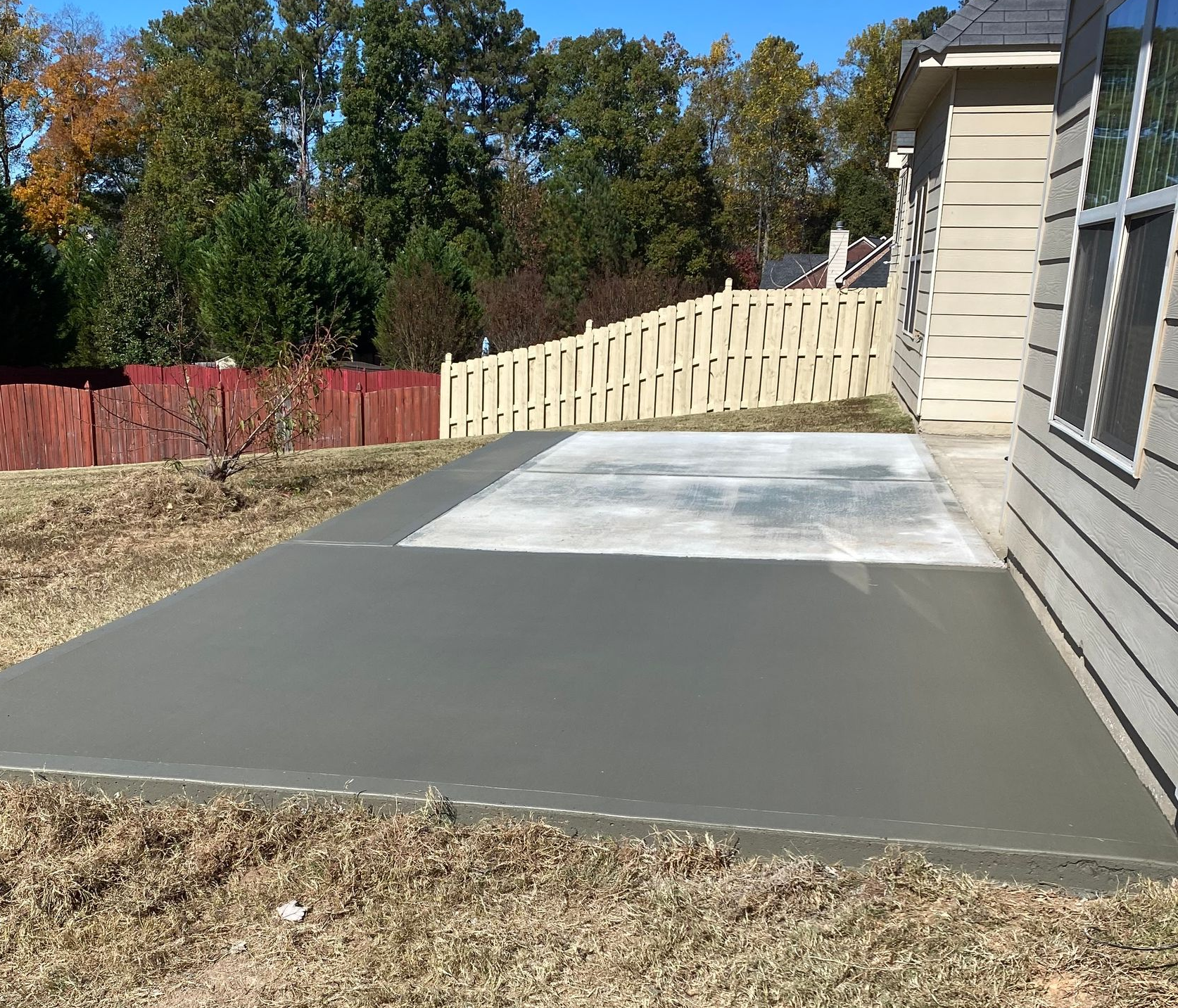 Newly poured concrete patio next to a house with a fence and trees in the background.