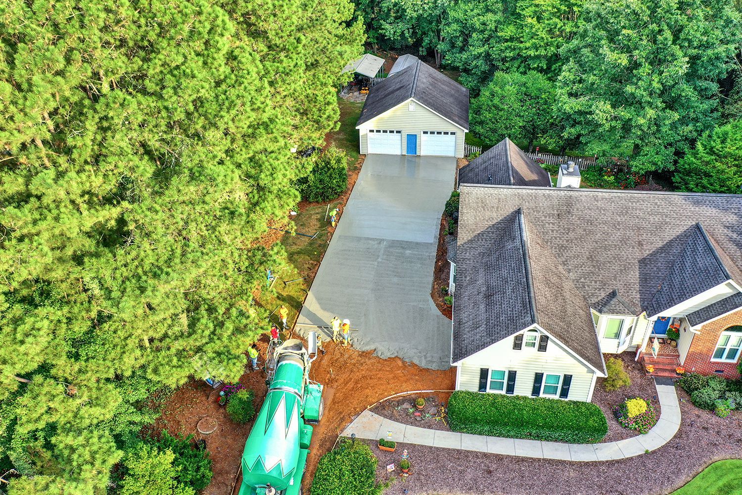 Aerial view of a house with a long driveway leading to a detached garage. A green cement truck is in the foreground.