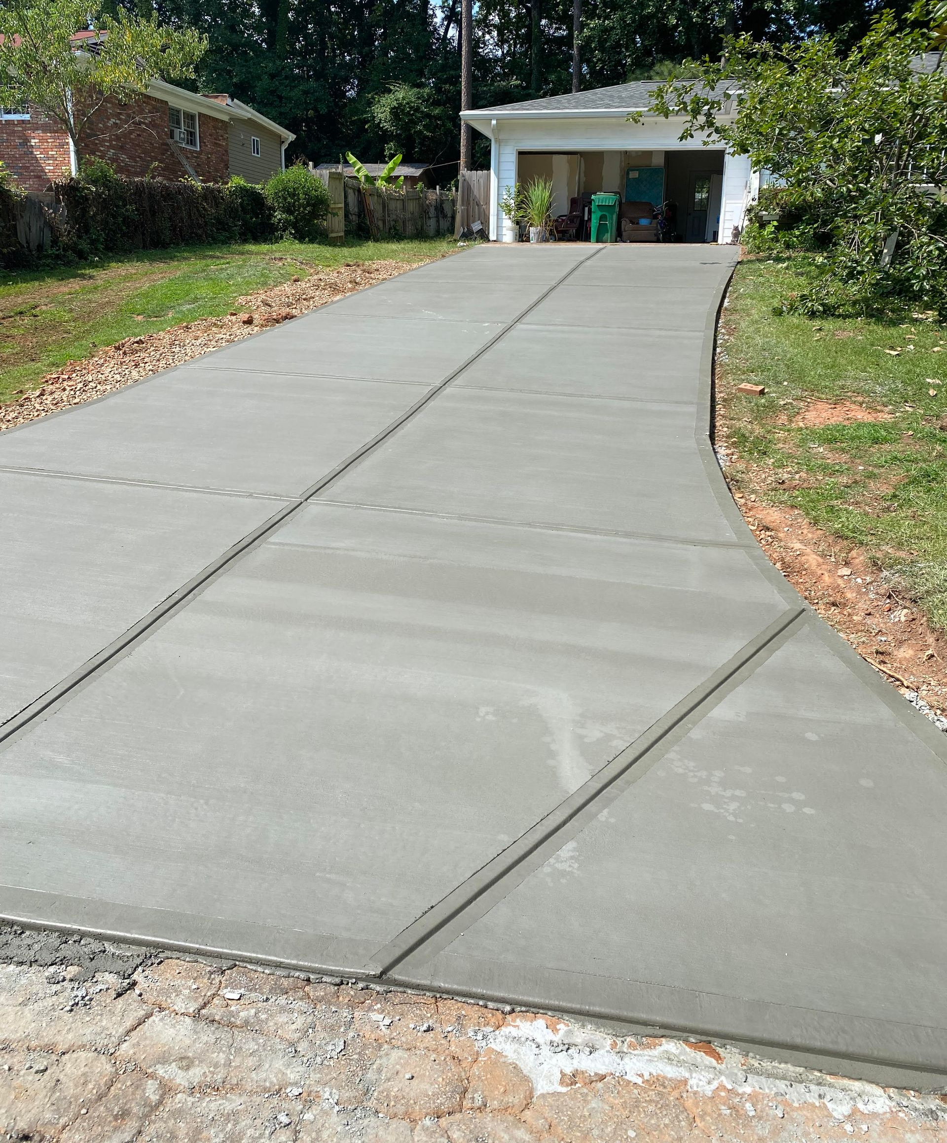 New concrete sidewalk under construction, blocked by yellow caution tape. Black railing, dirt and grass visible.