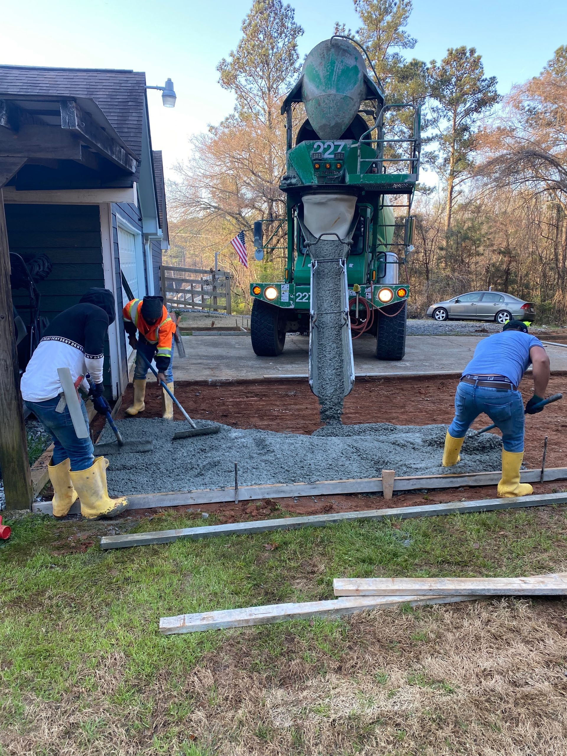 Workers pouring concrete from a truck into a form, near a building. Outdoor setting, overcast.