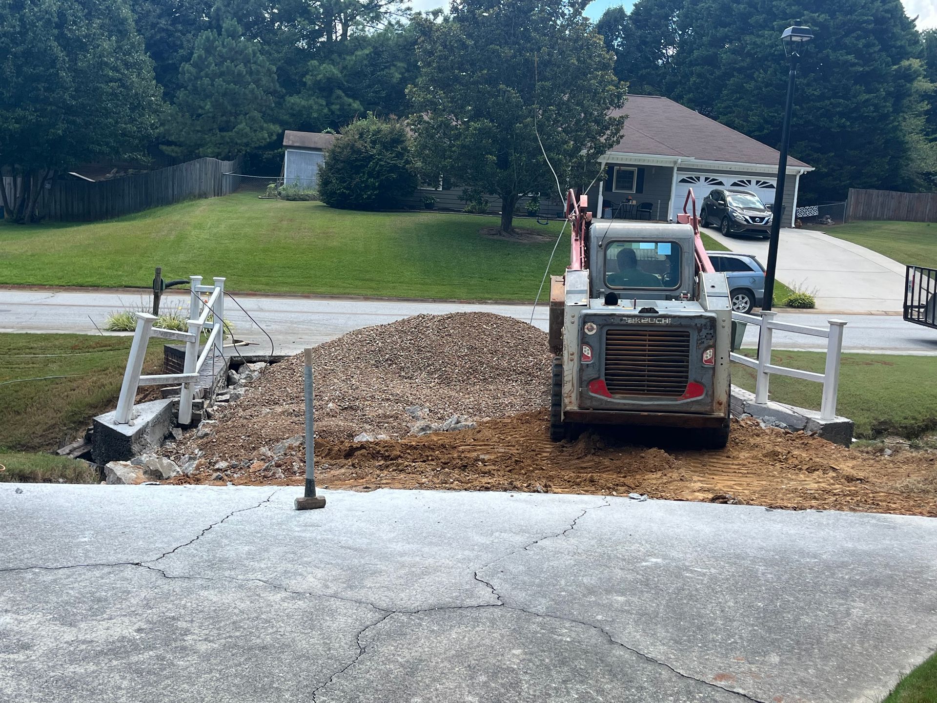 Skid steer loader pushing pile of gravel over destroyed bridge. Residential area.