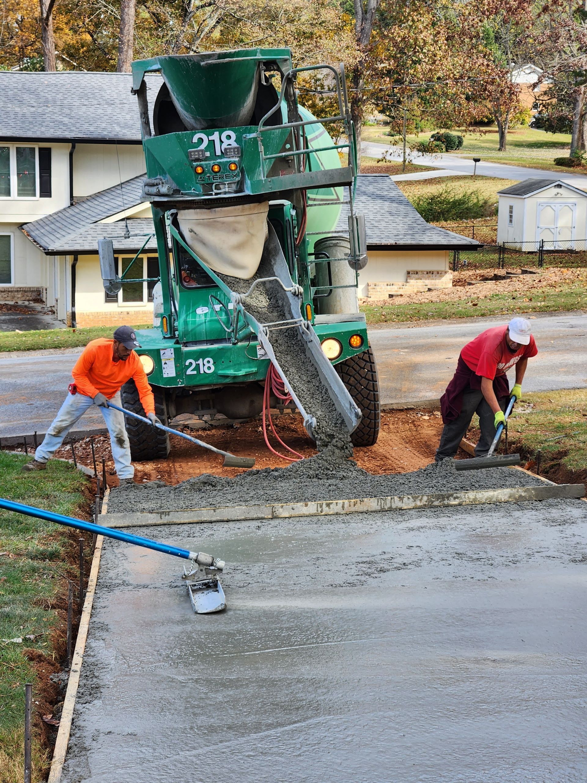Concrete being poured into a driveway by a cement truck with two workers using tools to spread it.