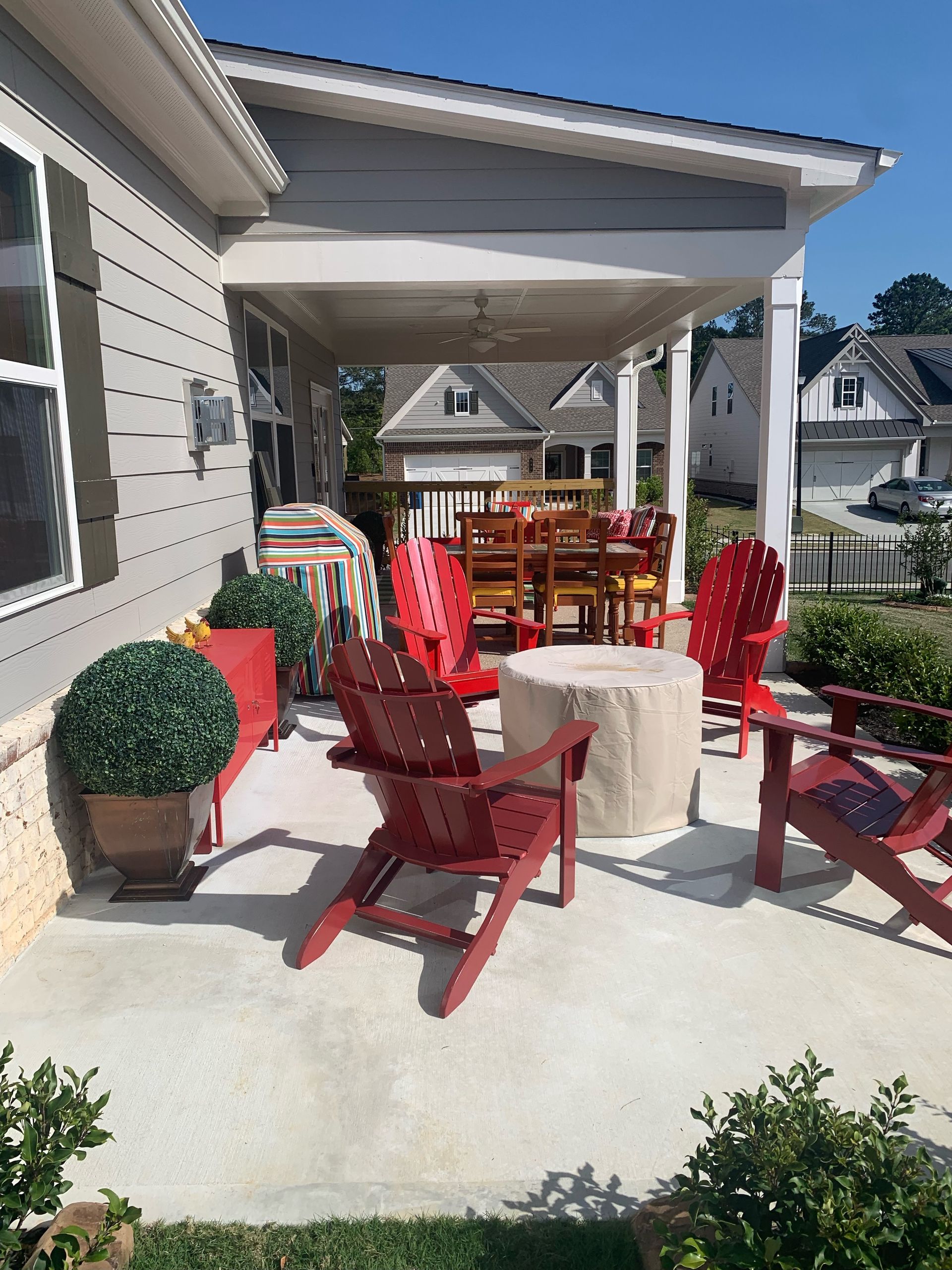 A covered patio with red Adirondack chairs and a fire pit, near a house.
