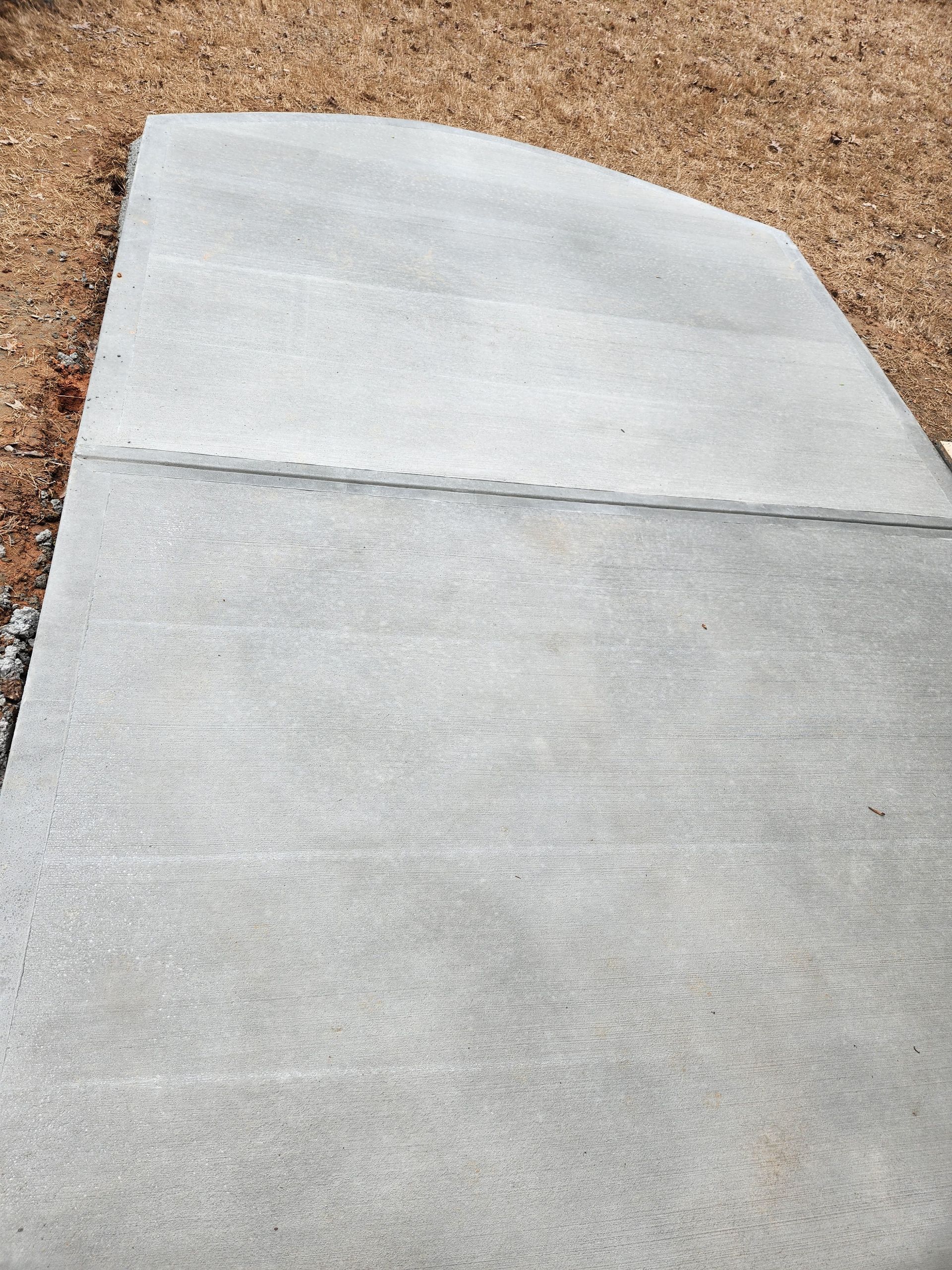 Newly poured gray concrete sidewalk with a curved edge.