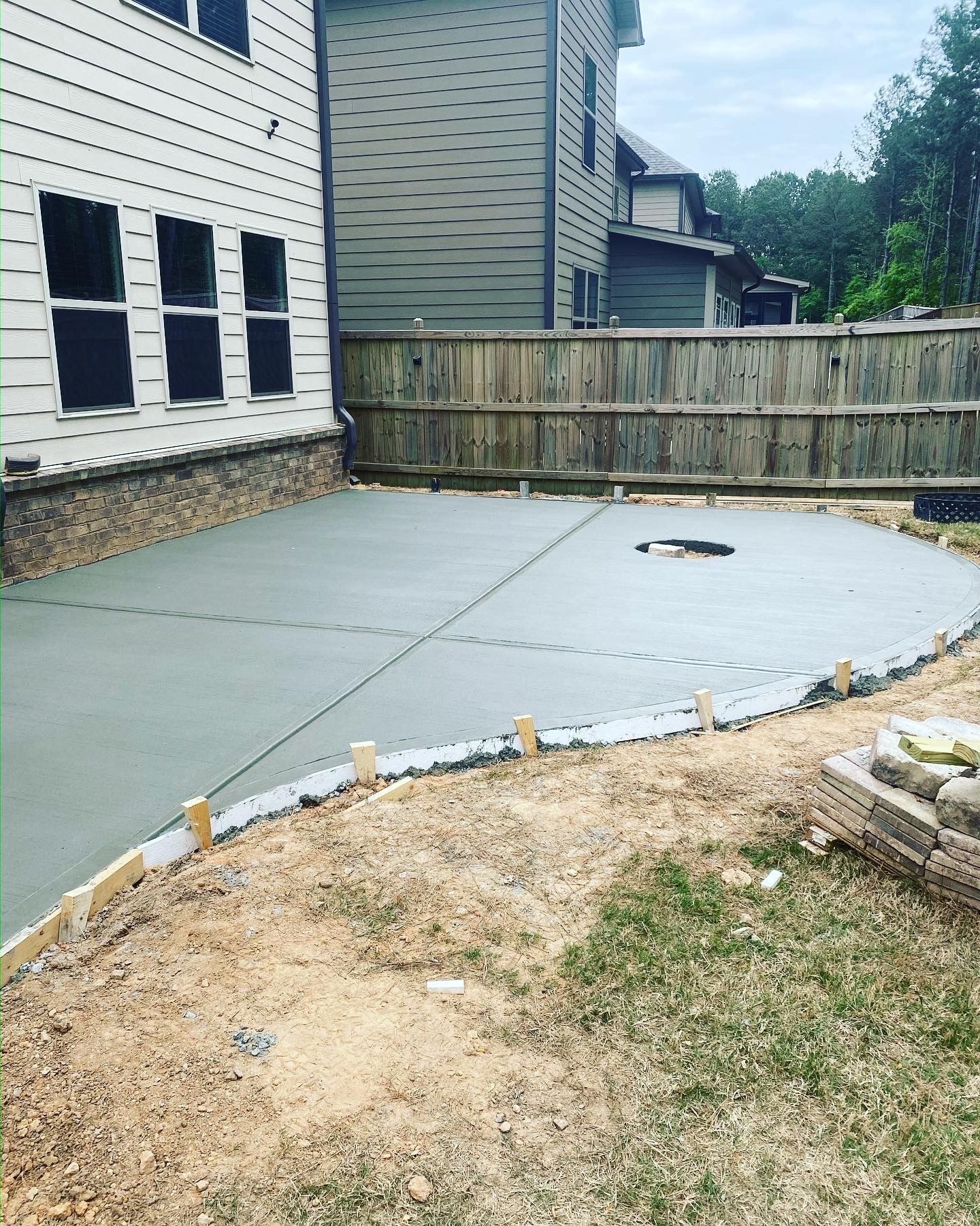 Newly poured concrete patio in a backyard setting, next to a house and a wooden fence.