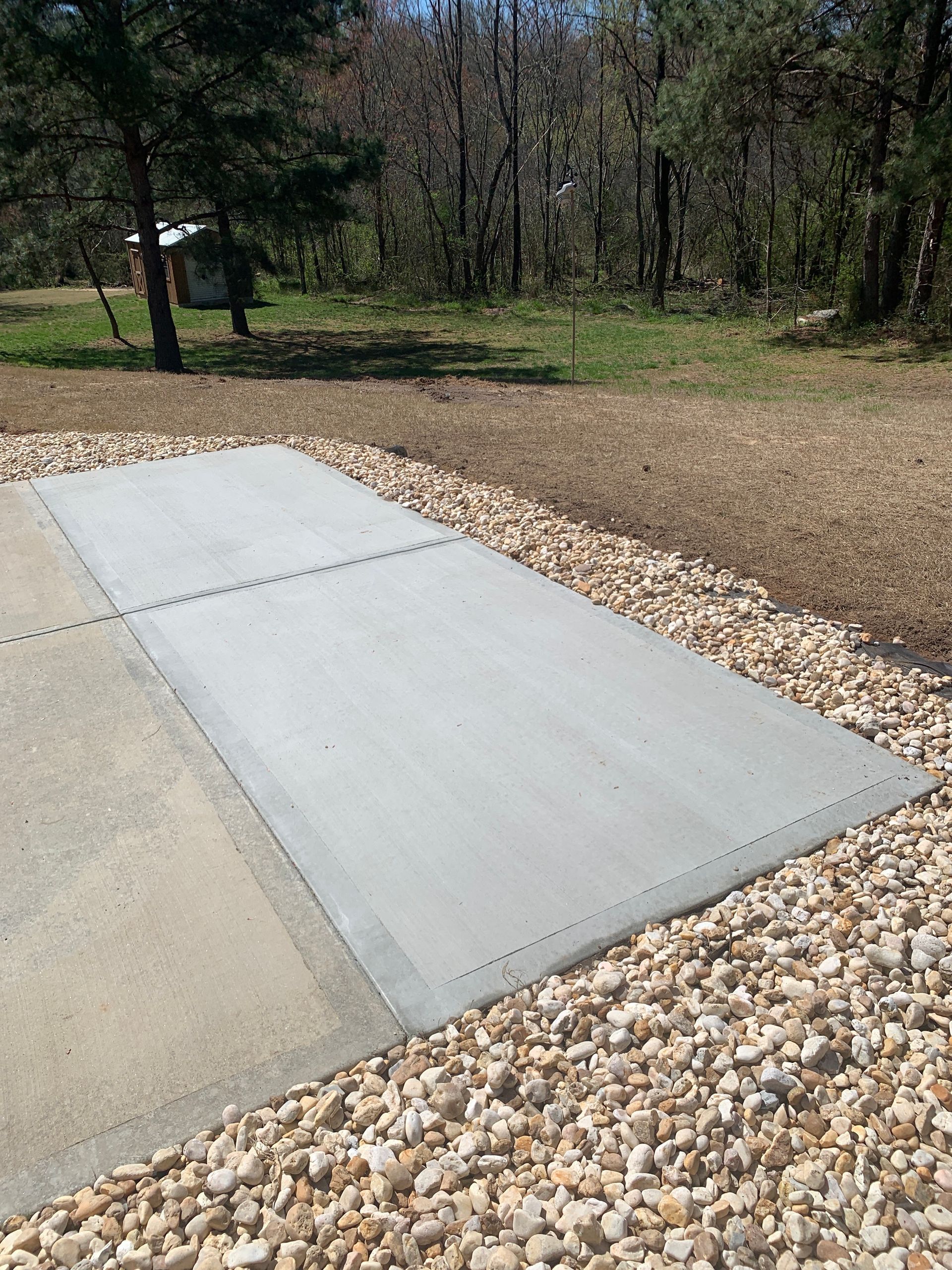 Concrete pads bordered by gravel, in a grassy outdoor setting, possibly a patio or parking area.